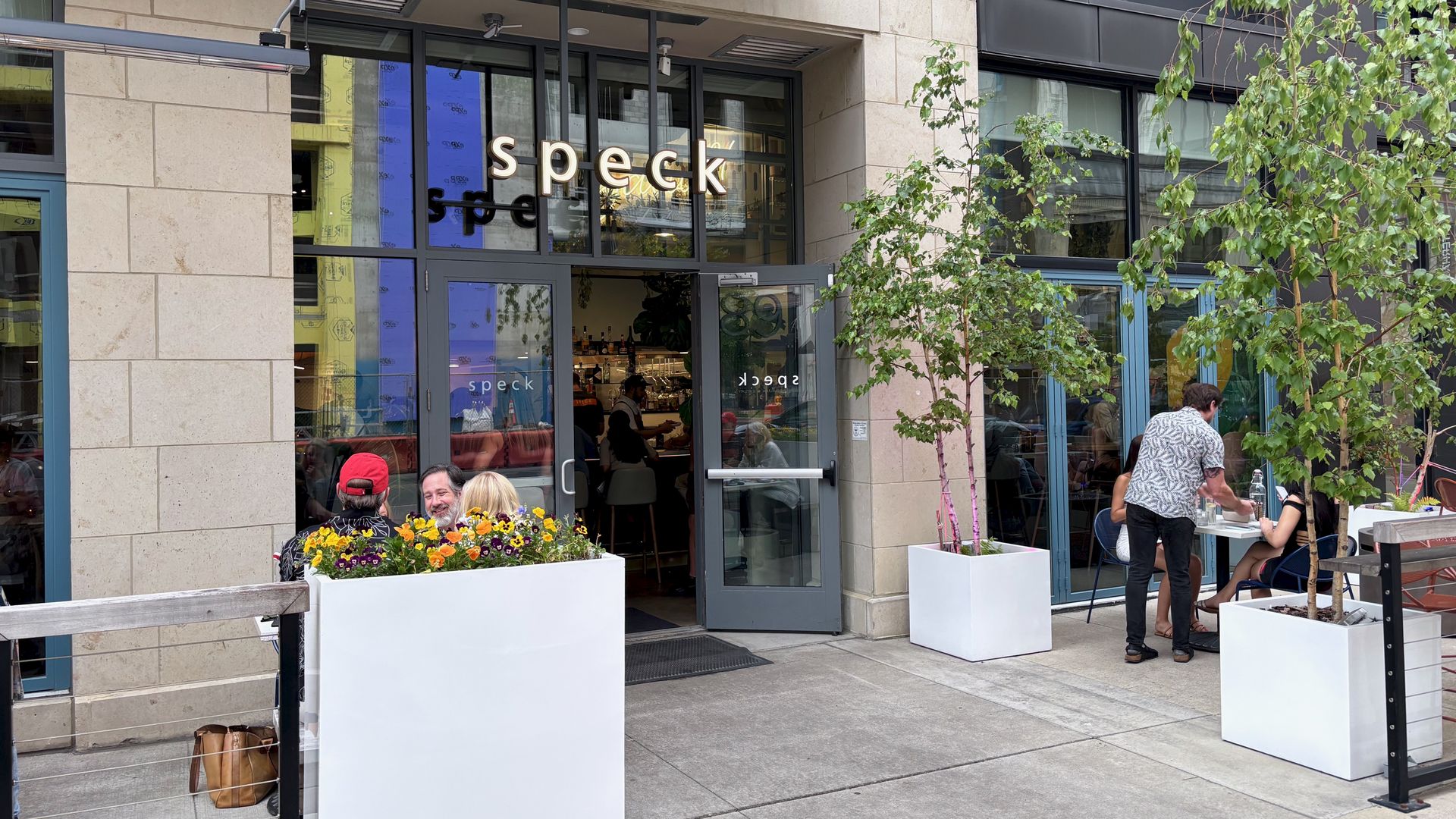 The exterior of the Speck restaurant, with a patio full of trees and flowers