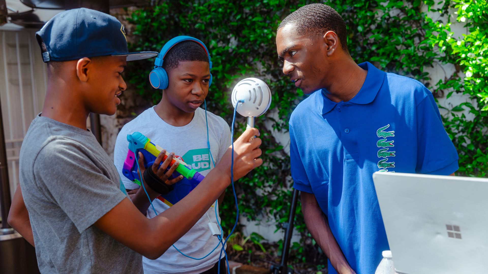 Three teens record audio while one of them speaks into a microphone.