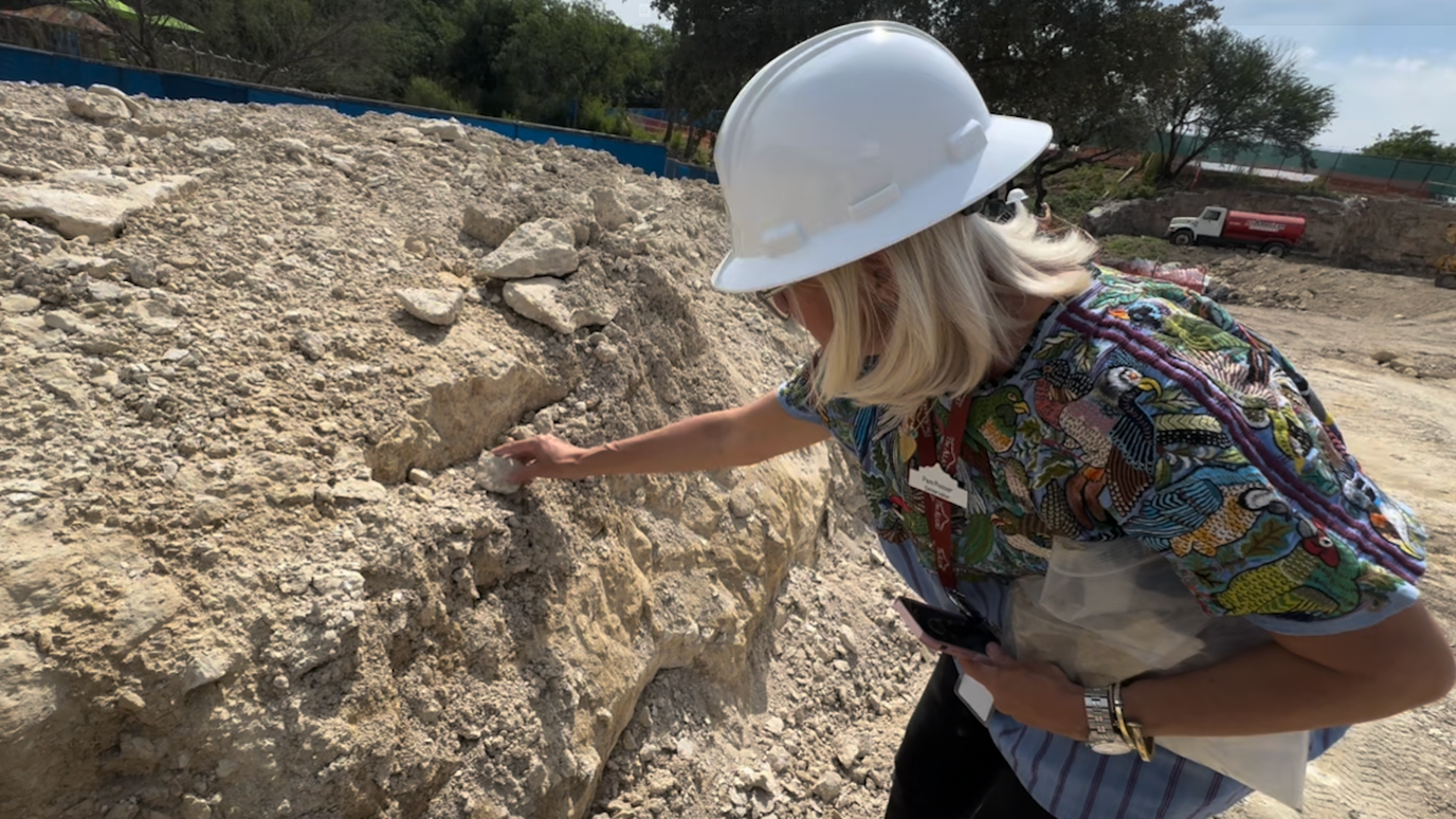 A woman wearing a hard hat examines a bed of rocks.
