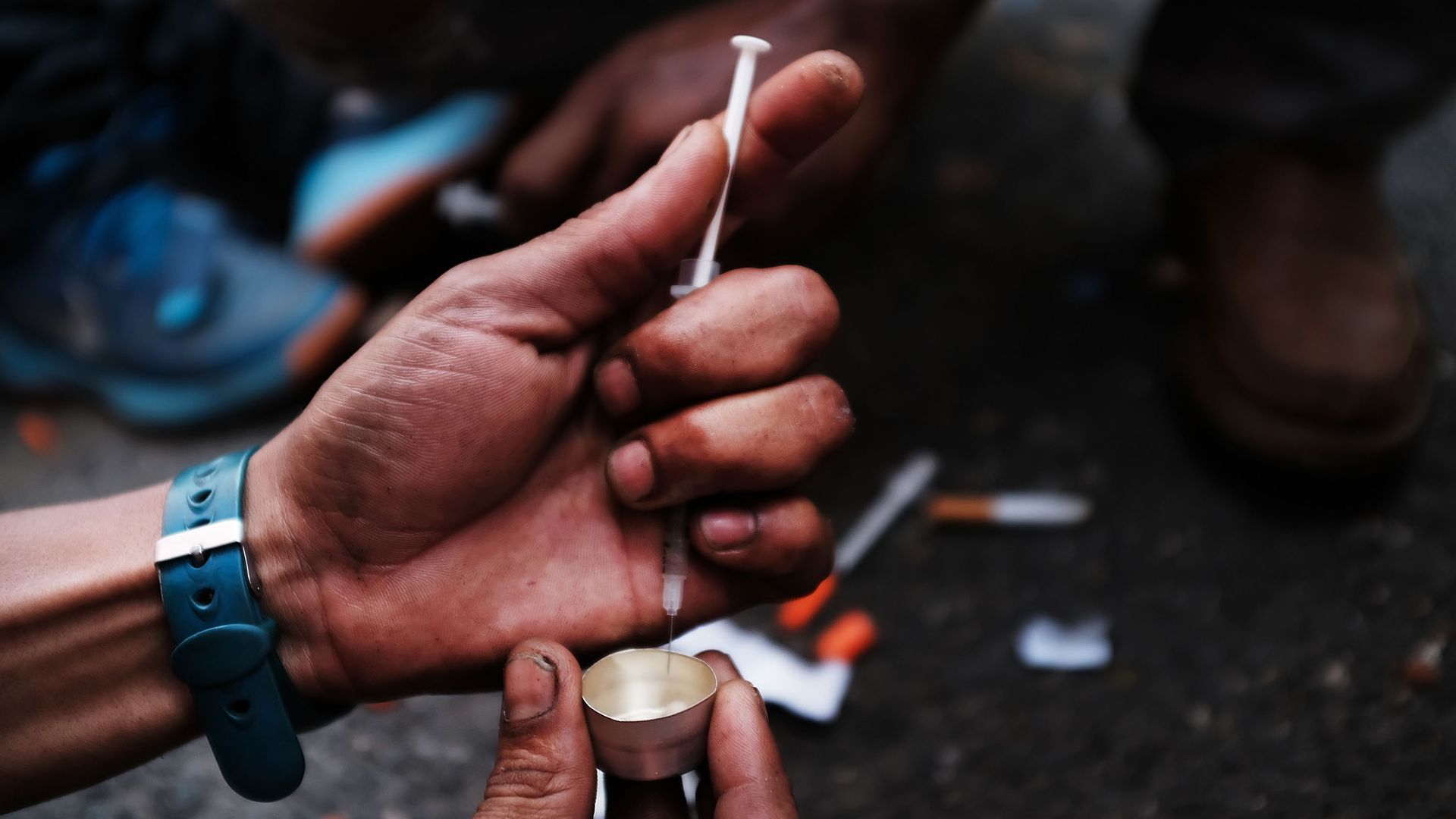 Photo of a heroin user's outstretched hand, holding a needle and preparing to shoot up