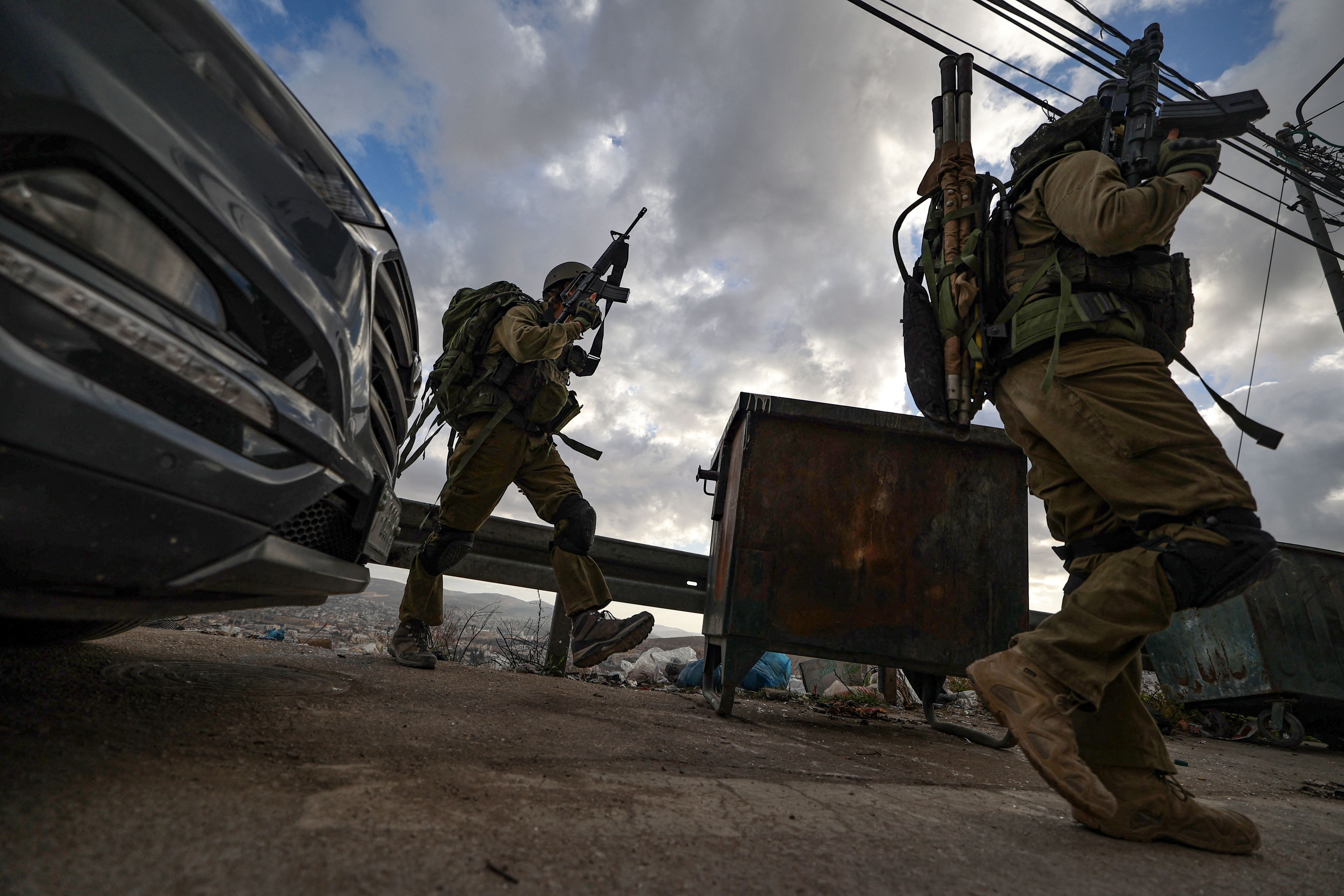 Soldiers holding up weapons and walking down a street in the West Bank. 