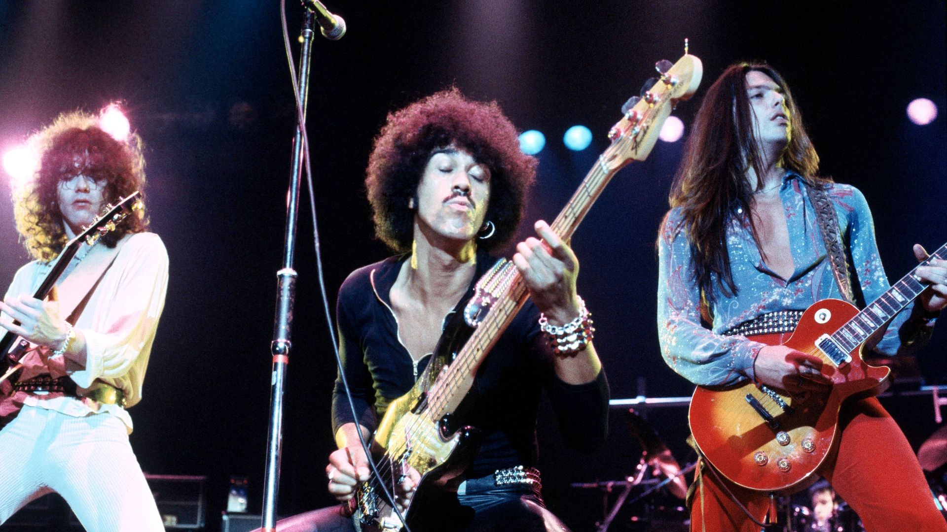 The three members of 1970s rock band Thin Lizzy perform on stage.