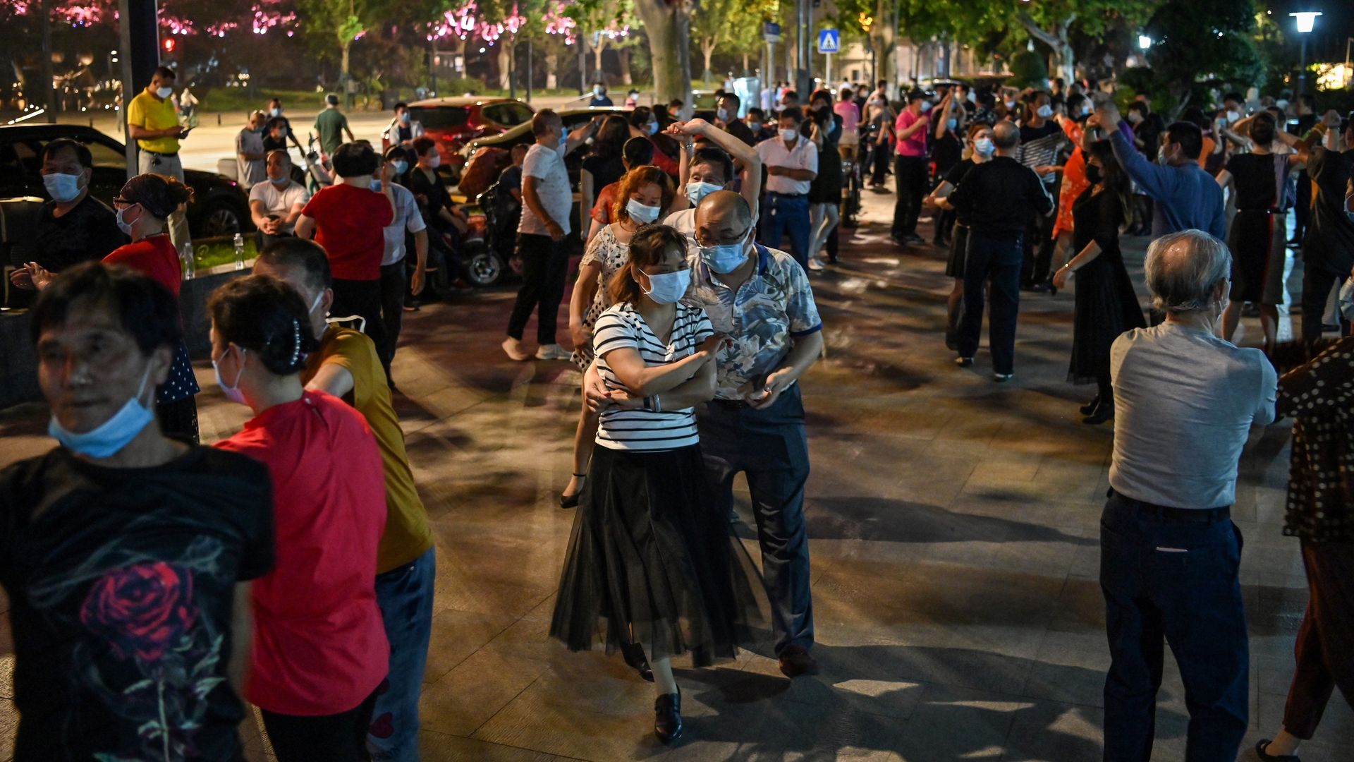 In this image, a man and a woman dance together outside while wearing face masks