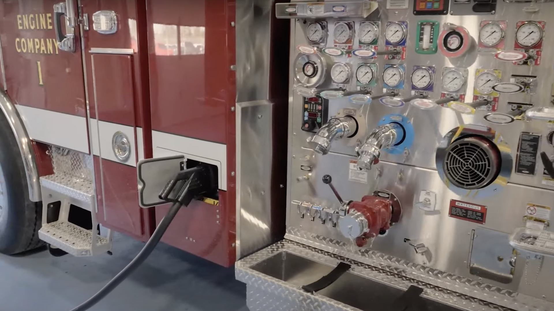 A red fire truck has a black cord plugging into it