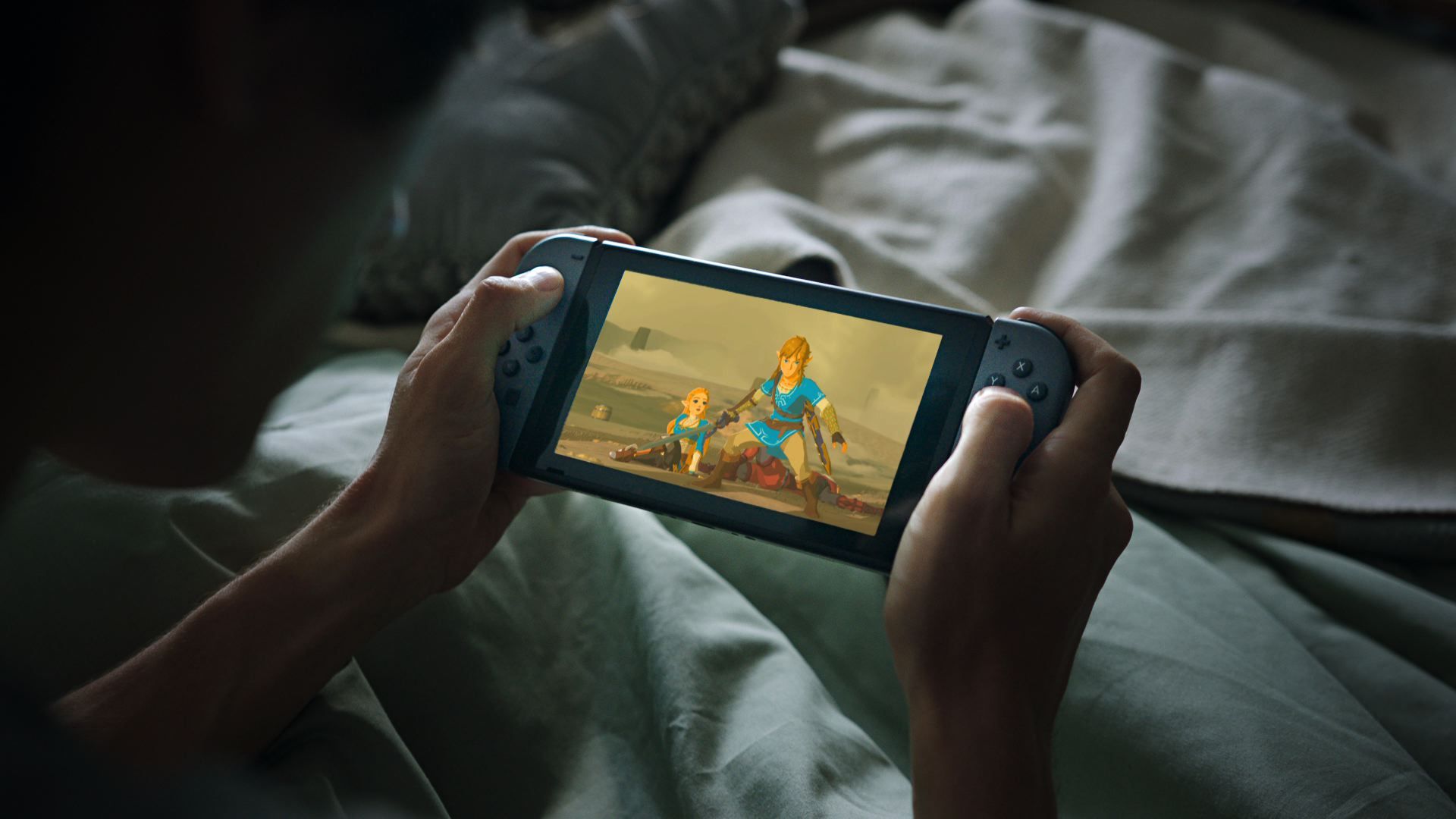 A person holds a Nintendo Switch system while laying in bed