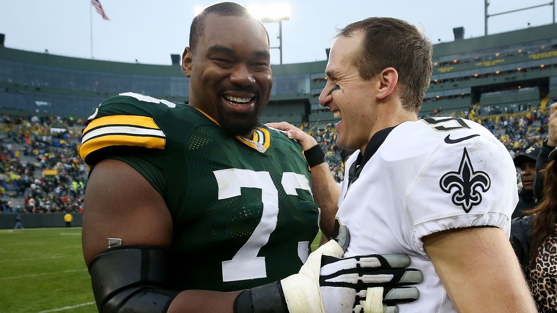 Jahri Evans, wearing a Green Bay Packers jersey, greets Drew Brees, who wears a Saints jersey, on a football field. Both smile.