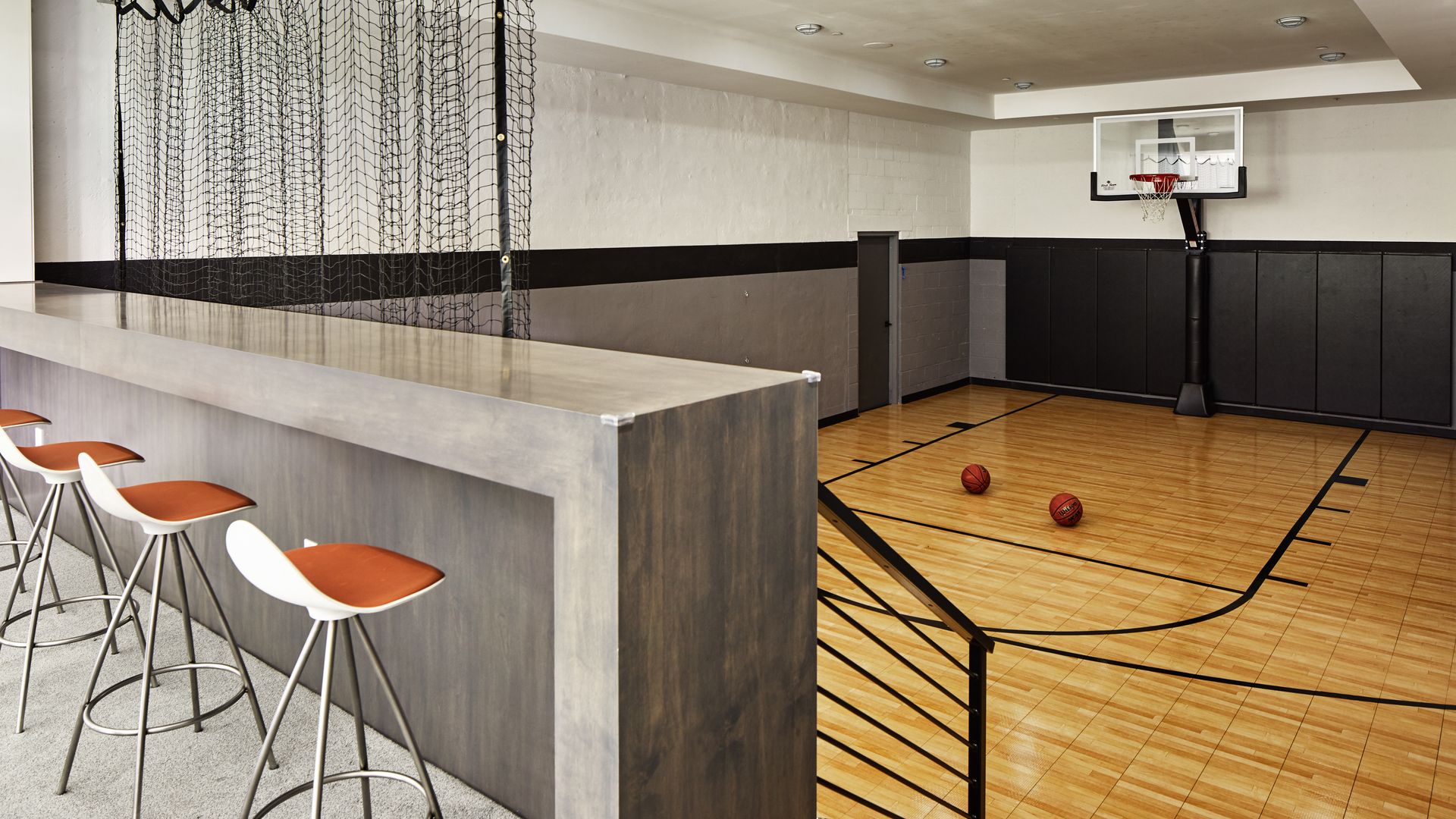 A modern bar with seating overlooks an indoor sports court.