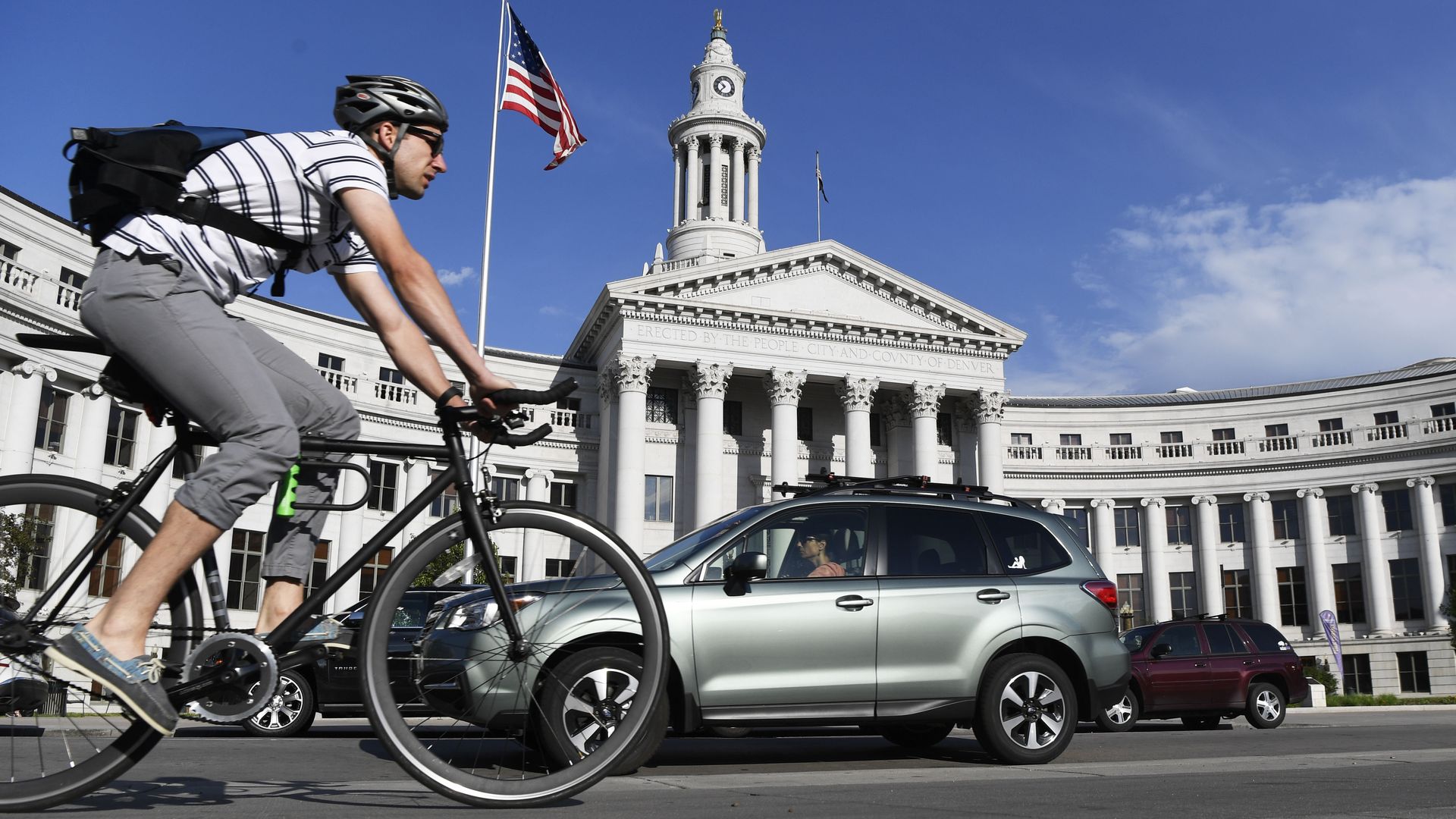 A man rides his bike next to a car near Denver city hall. 