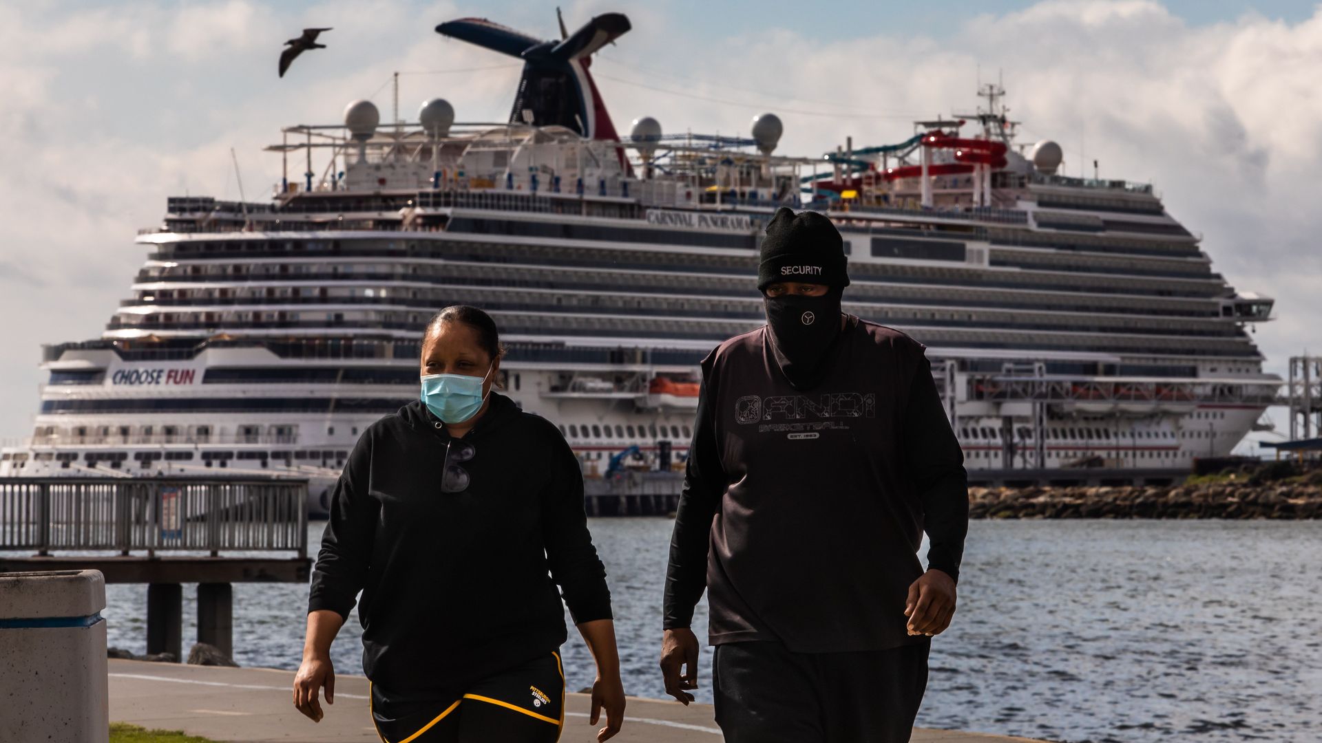  A couple wearing face masks as a preventive measure against the spread of the COVID-19 Coronavirus, walk at the Marina Long Beach with Cruise Ships docked at the port 