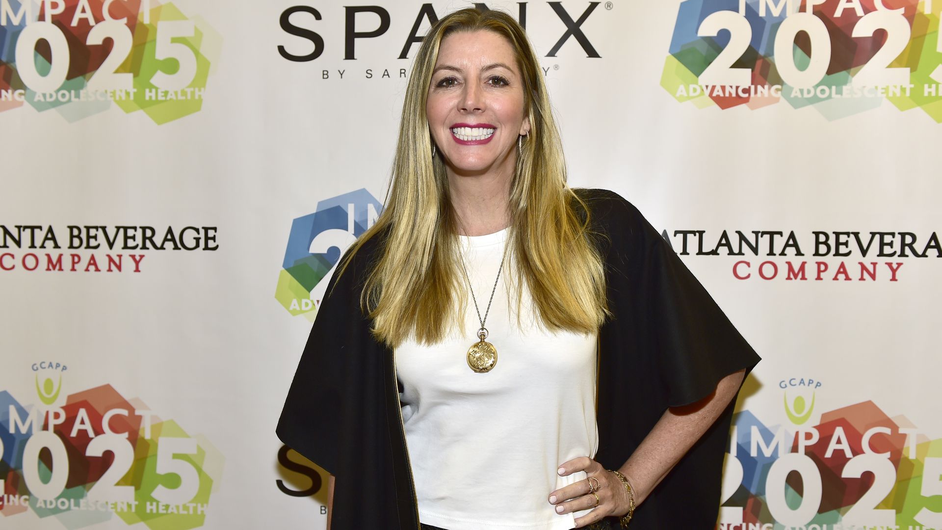 An individual with blonde hair poses and smiles for the camera standing in front of a backdrop that says "Spanx" and "Atlanta Beverage Company"