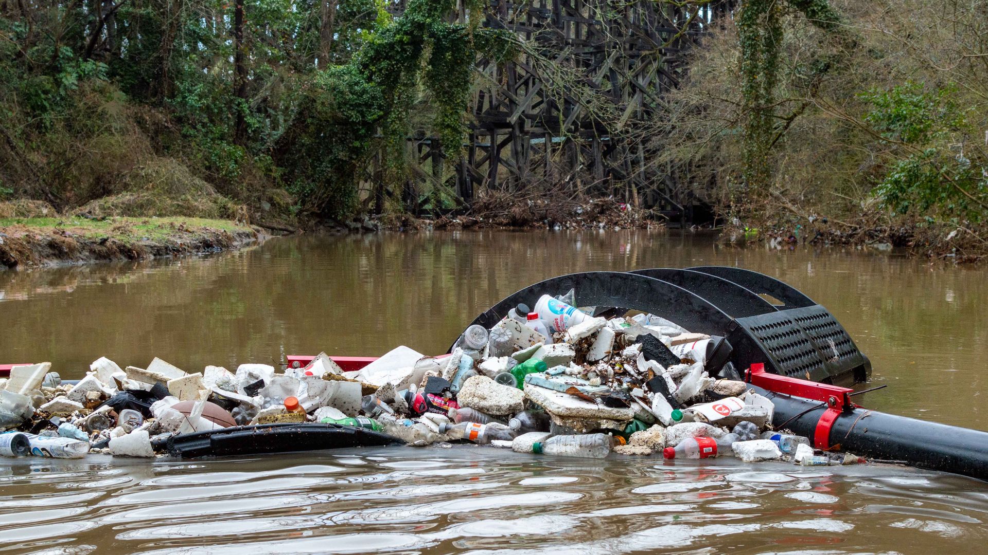 A photo of a creek with a device that filters bottles and other floating trash  