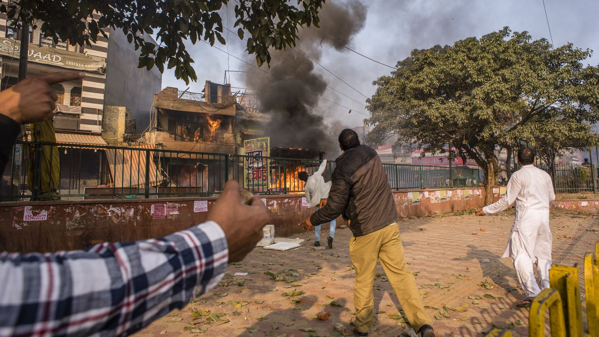 Protesters supporting a new citizenship law throw stones at the burning houses and shops of those who are opposing the law 