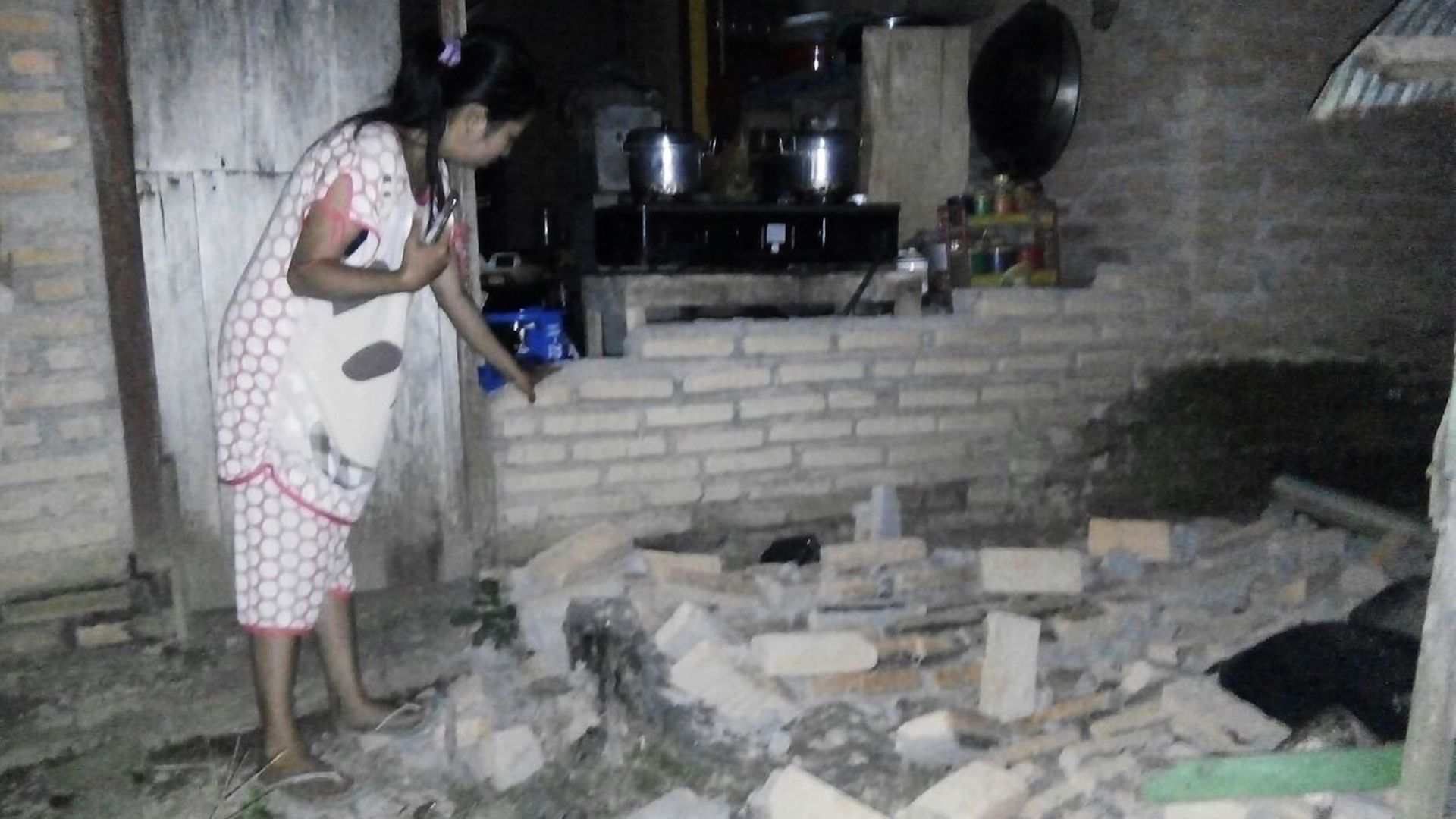 A resident is seen beside the collapsed brick wall of her house at Tobadak village in Central Mamuju, western Sulawesi province, on September 28, 2018, after a strong earthquake hit the area. 