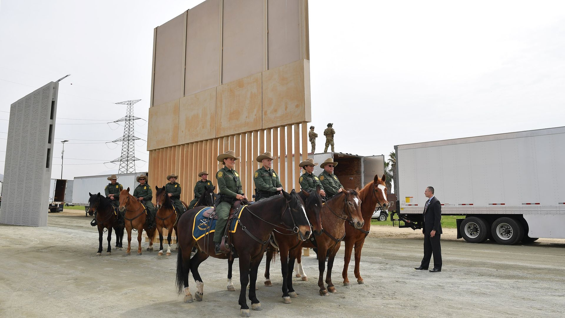 Mounted Border Patrol agents on horseback in front of a prototype of Trump's border wall