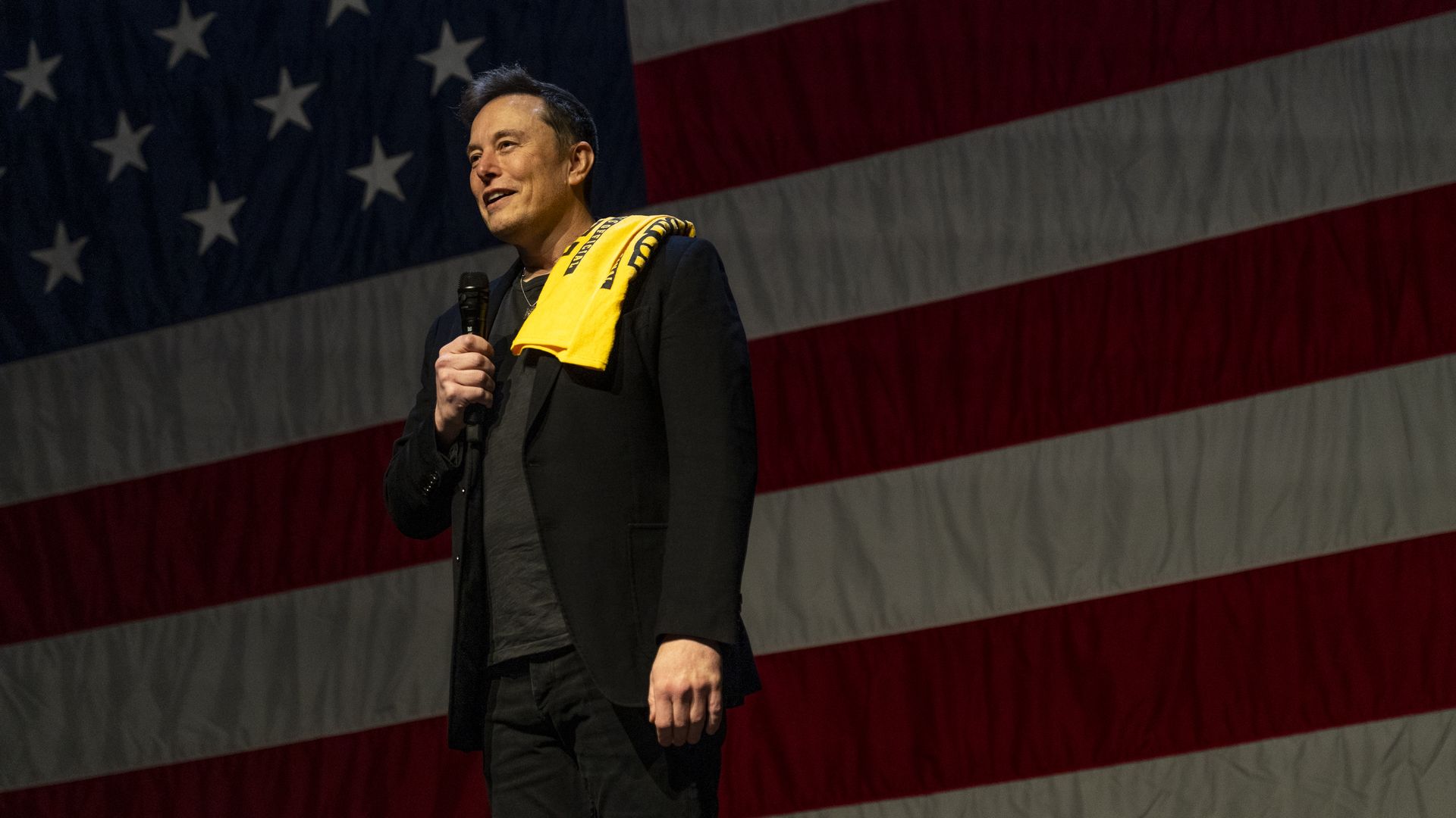 Elon Musk at a Trump rally standing in front of an American flag.