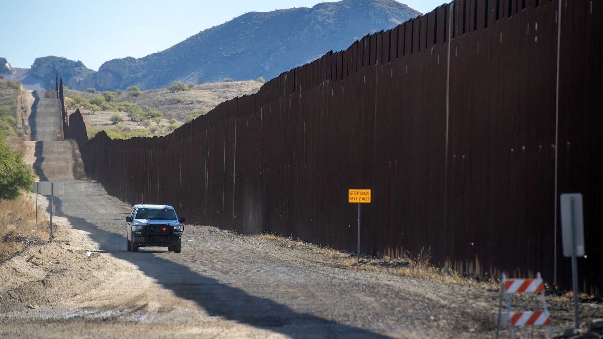 A border patrol vehicle driving along border wall. 
