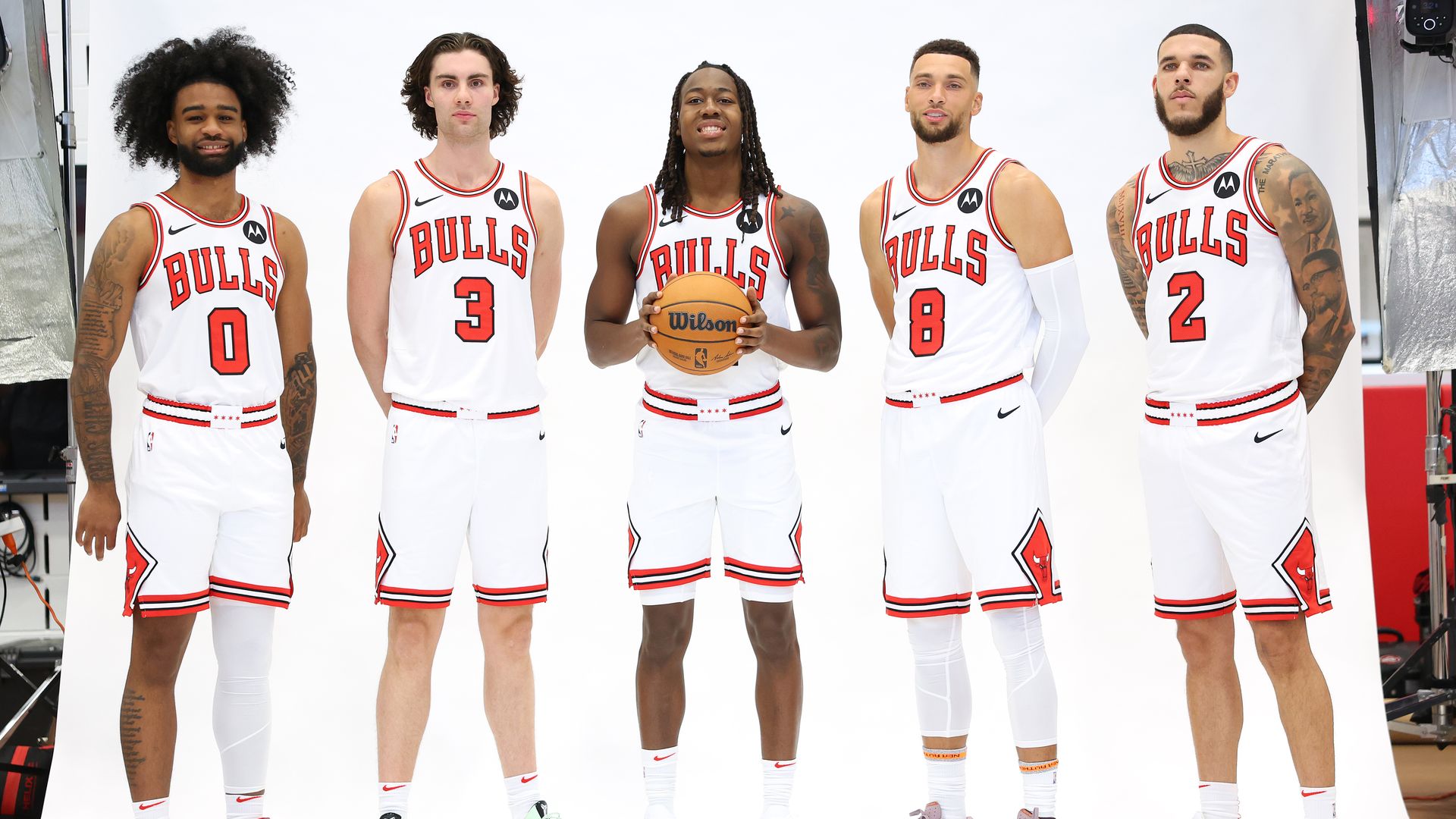 Photo of five men dressed in basketball uniforms holding a basketball posing for camera 