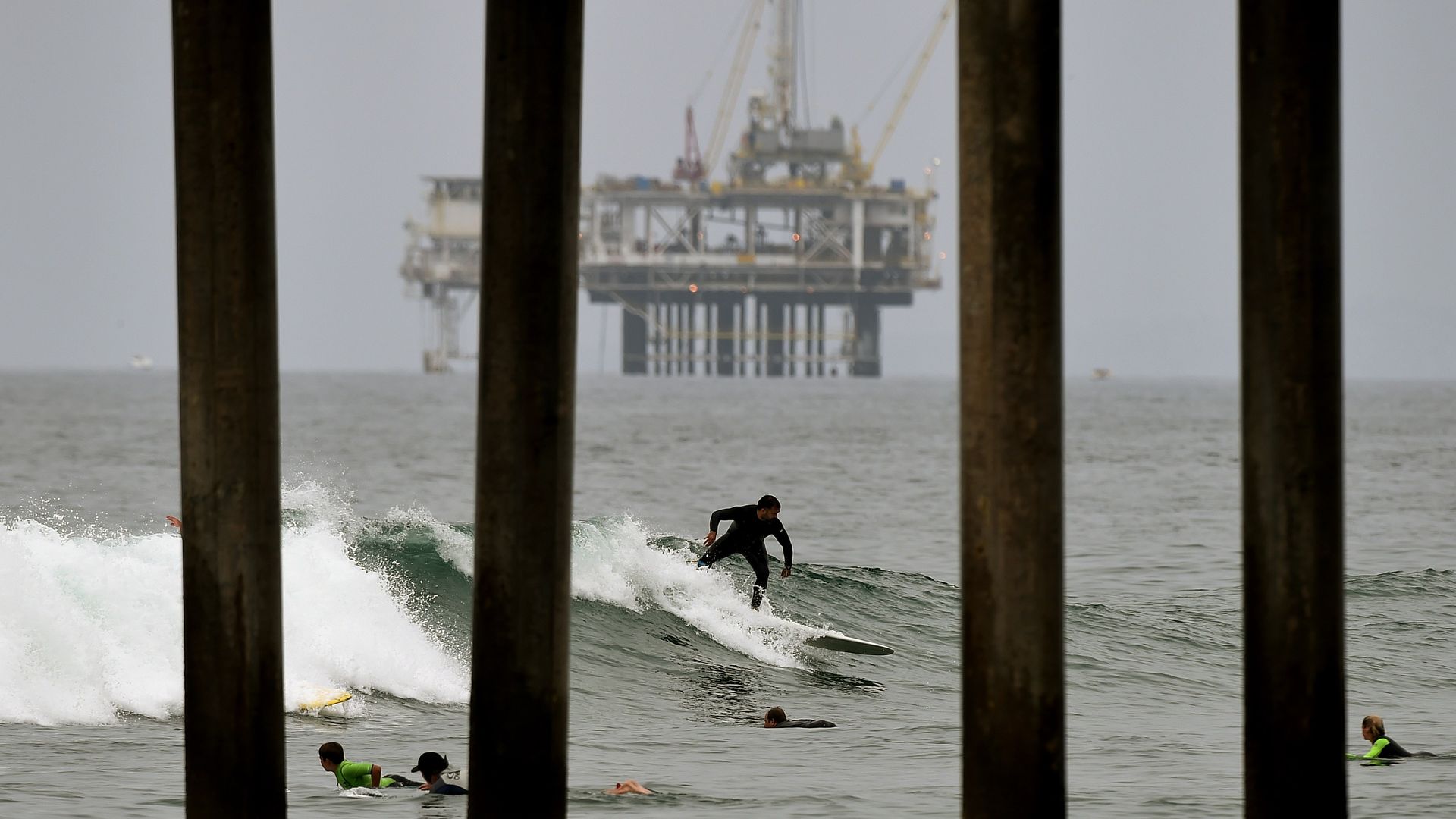 Someone surfing a wave with an oil rig in the distance