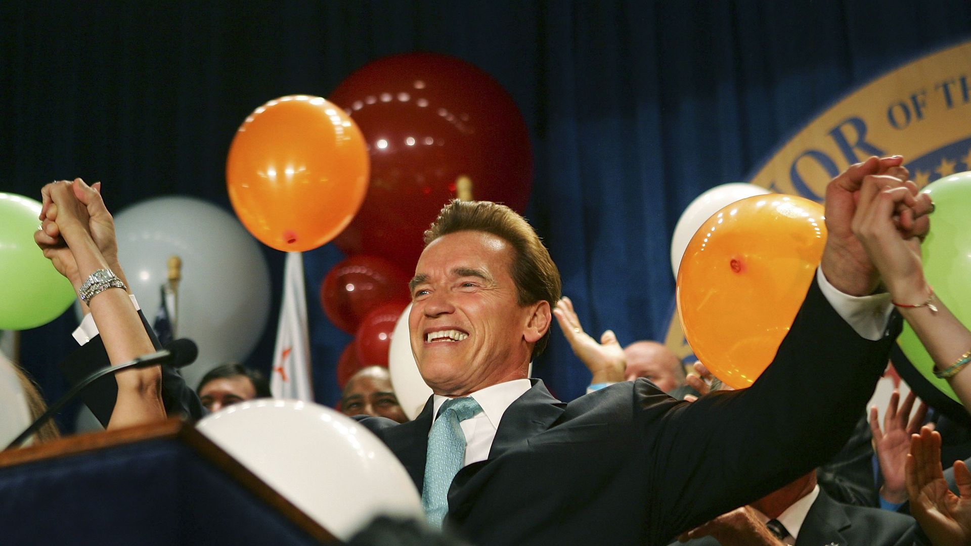 Schwarzenegger throws his hands in the air at a victory party