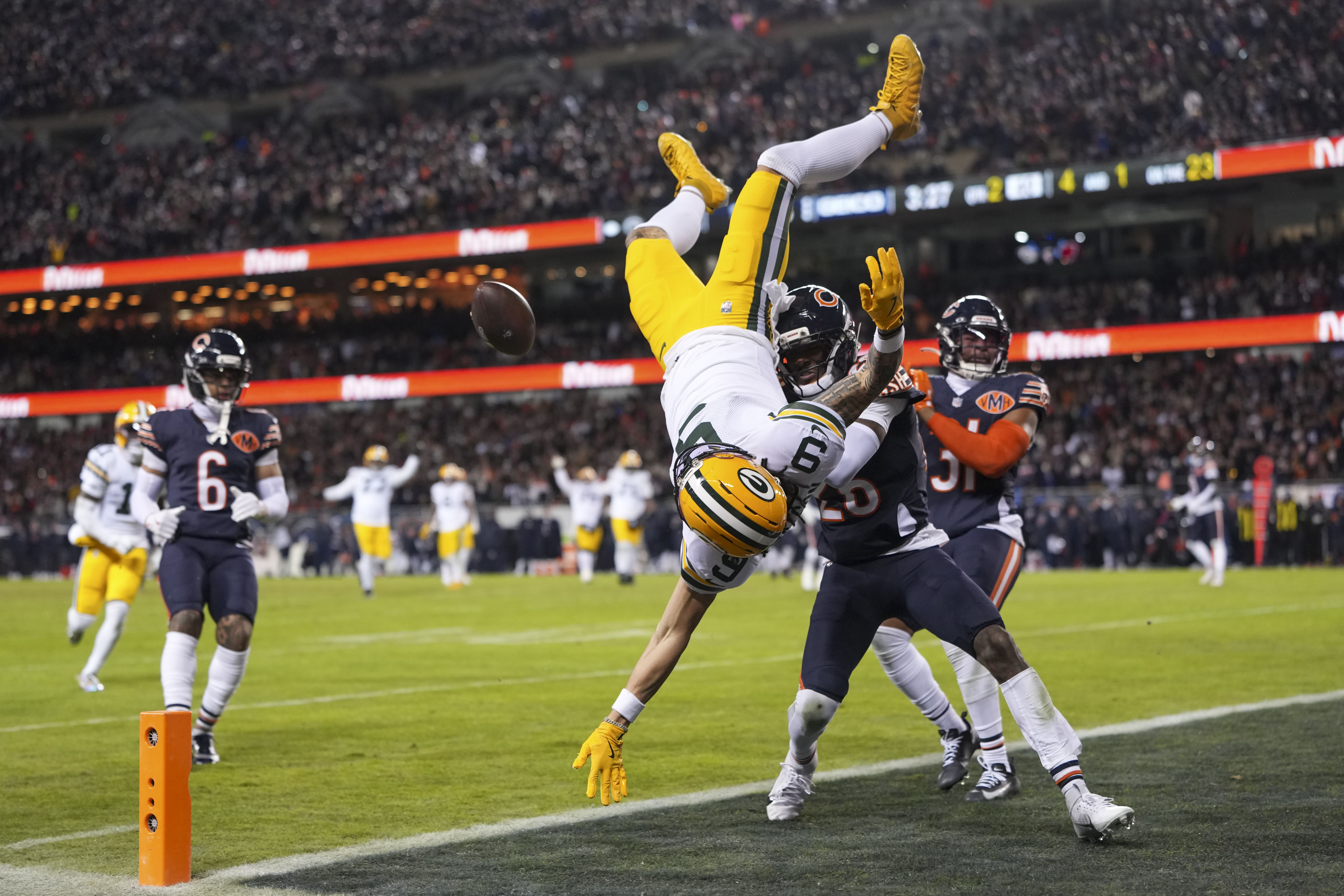 Green Bay Packers player flips midair near end zone as Chicago Bears defenders attempt to tackle during crowded stadium football game.