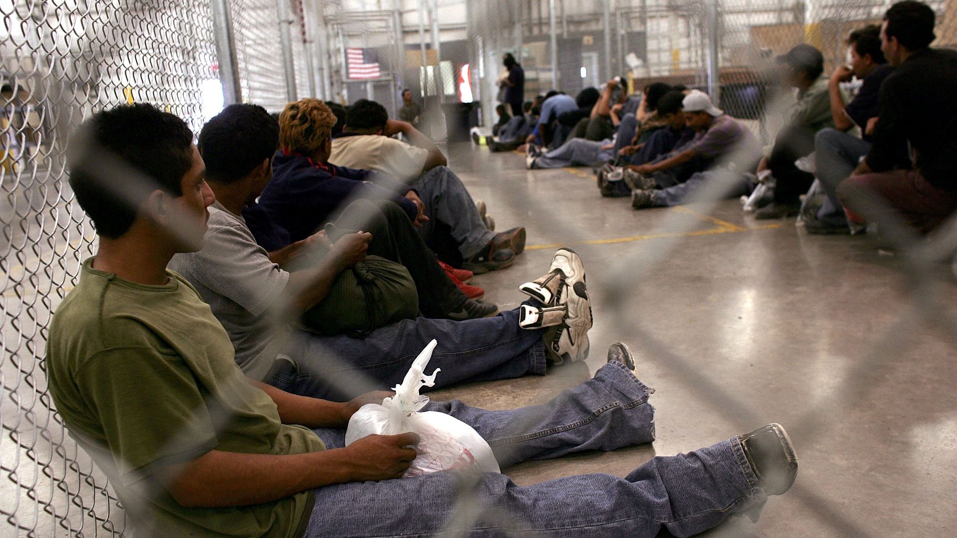 men sit on the floor behind chain link fence