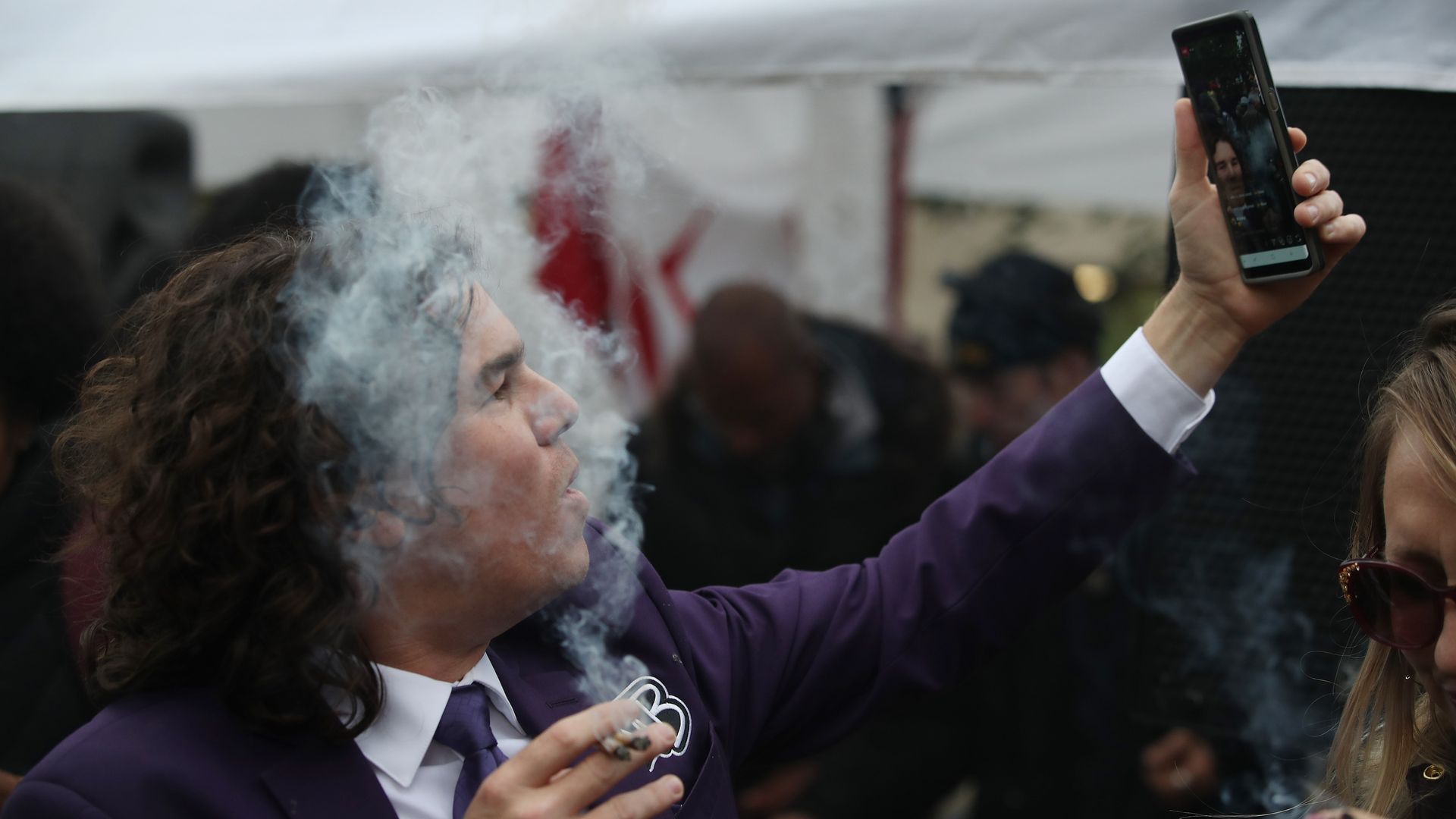 In this image, a man in a suit takes a selfie while smoking. 