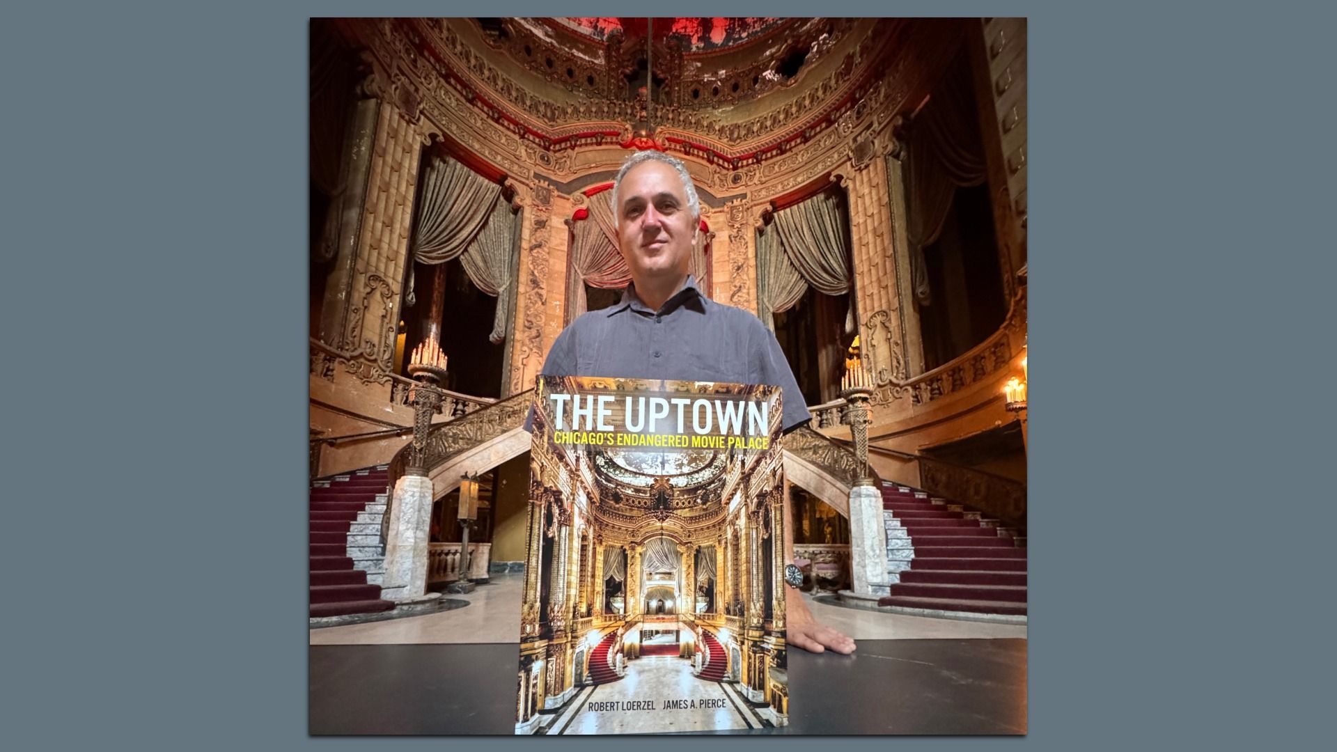 Man with gray hair stands in an ornate theater lobby holding a book titled "THE UPTOWN: Chicago's Endangered Movie Palace" in front of grand staircases with red carpet and intricate gold decor.