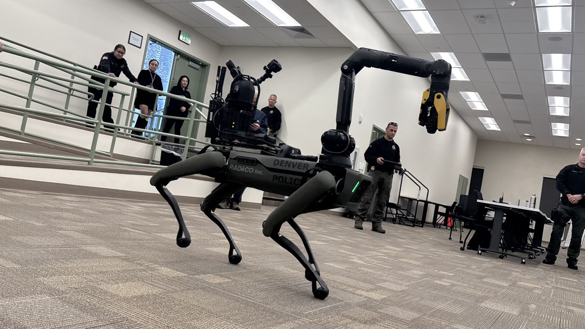 A robot dog with "legs" covered in a dark grey material, with a crane-like arm extending above it.