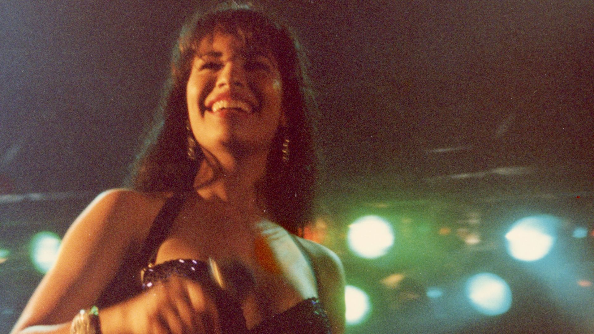 An archival photo of Selena smiling on a stage. 