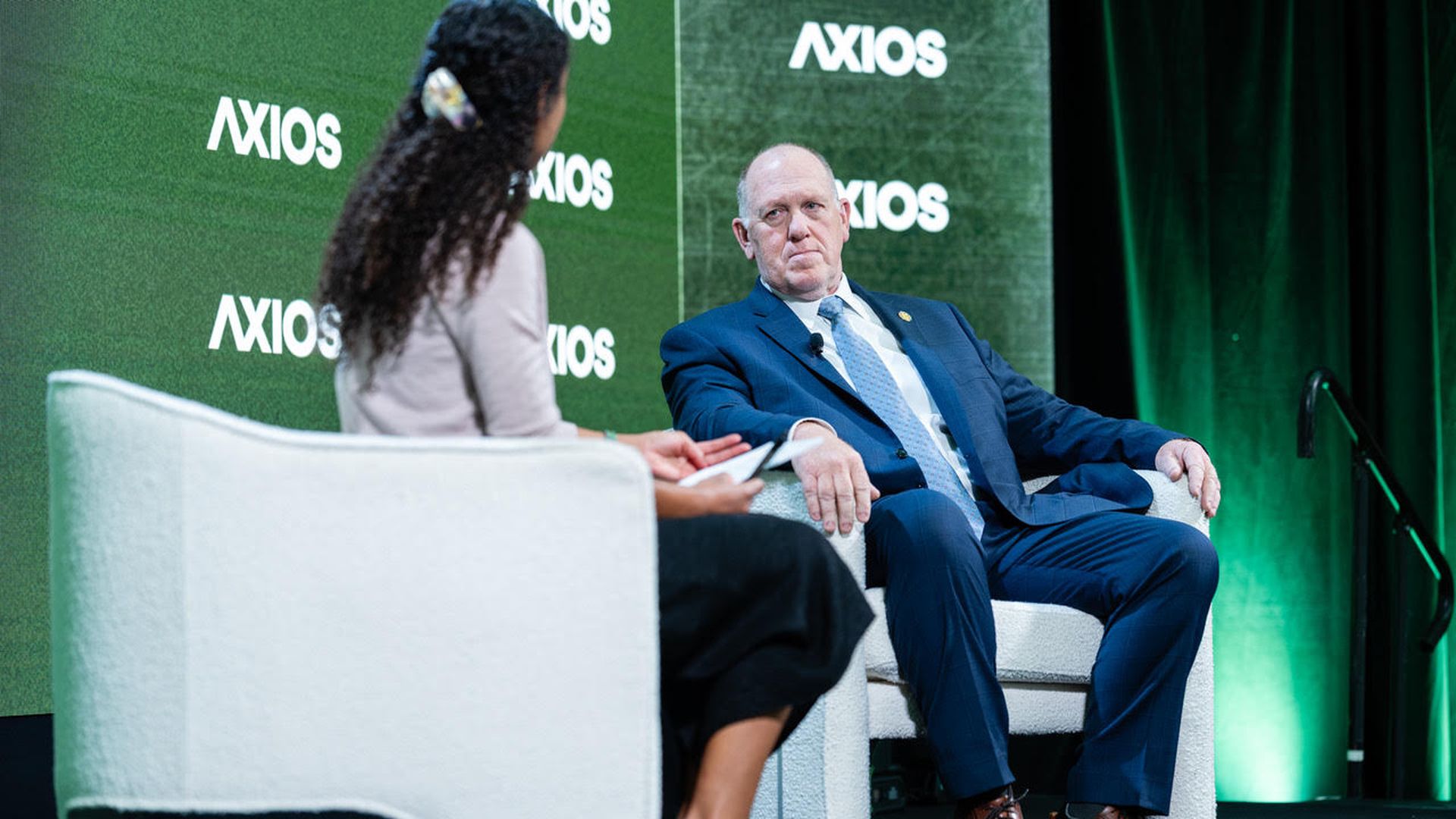 Tom Homan, wearing a blue suit and tie with a white shirt, is interviewed by Axios' Brittany Gibson in front of a green "Axios" screen. 
