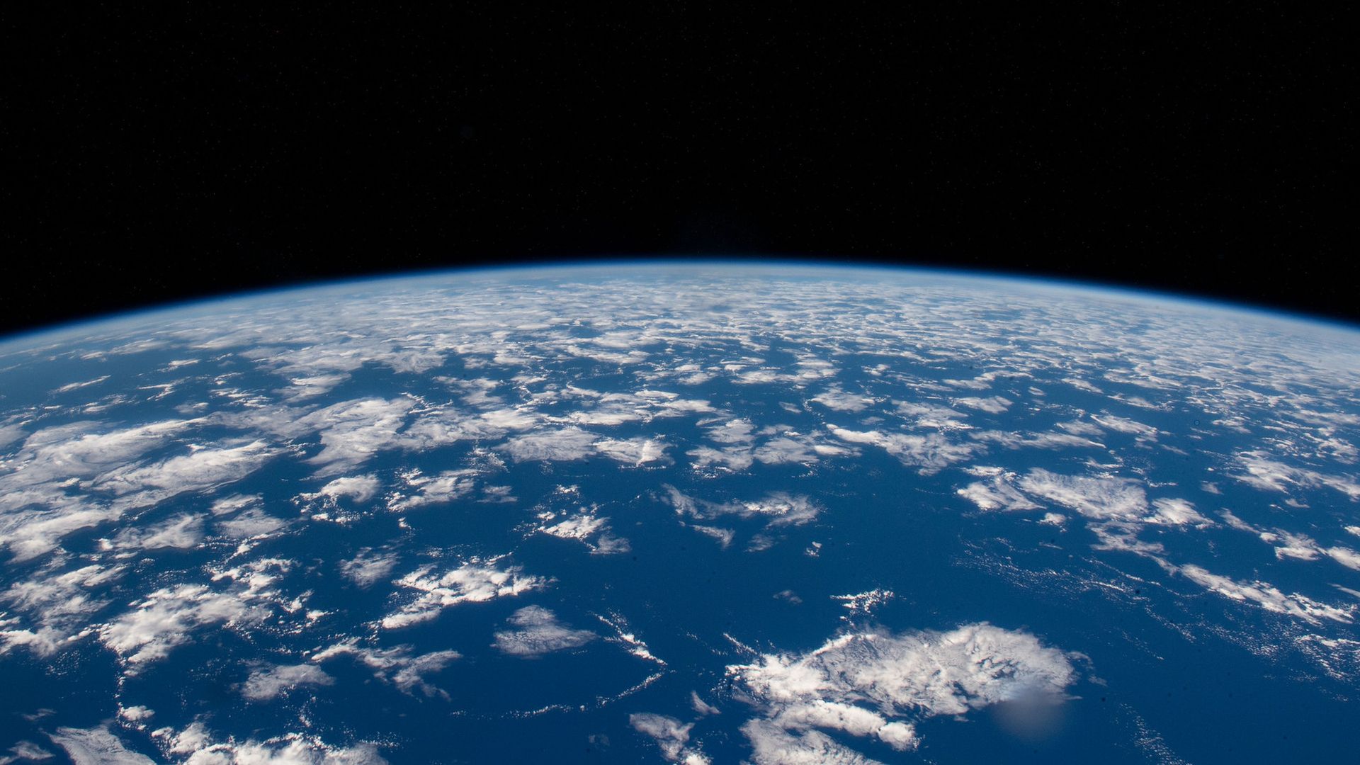 Earth's blue water with dappled clouds against the blackness of space.
