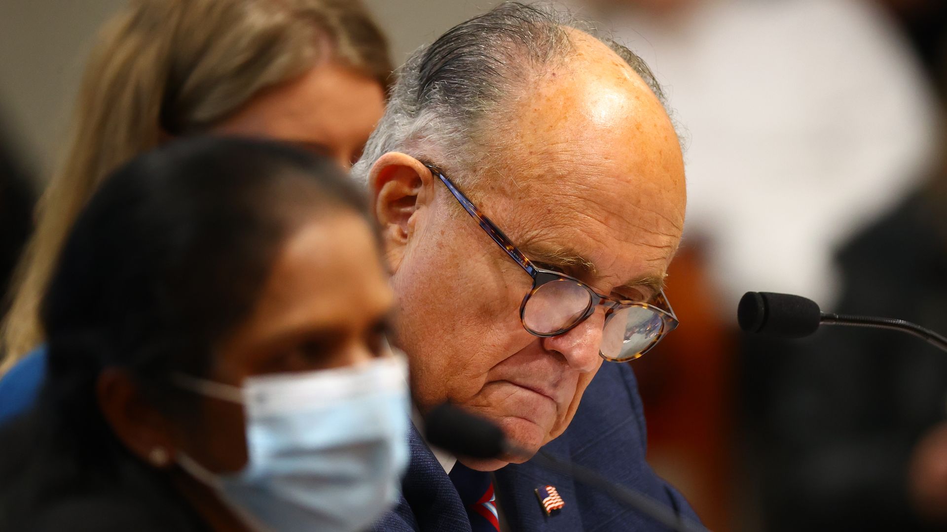 Rudy Giuliani sits next to a woman wearing a mask 