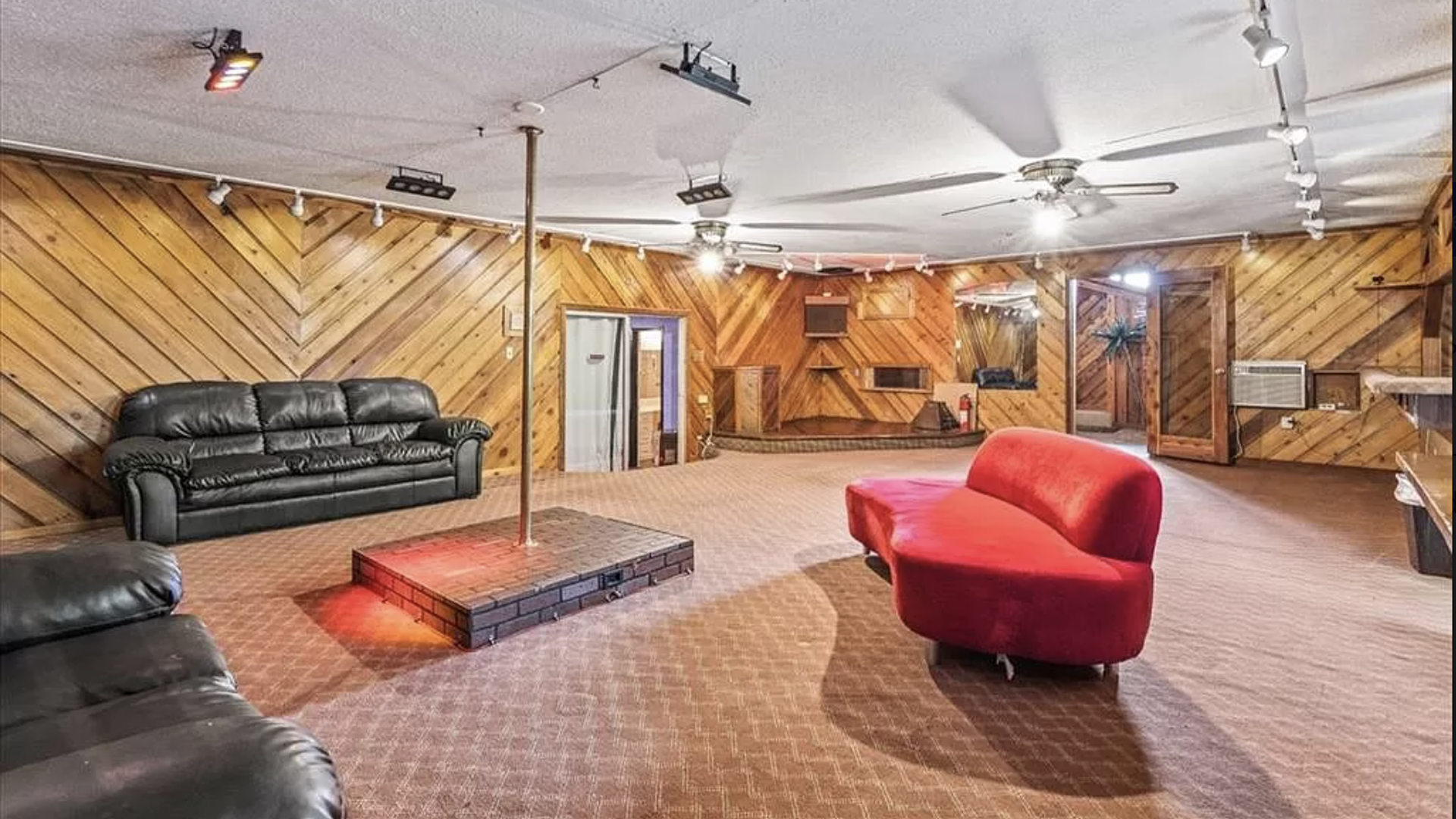 A wooden-paneled room and three couches facing a stripper pole.