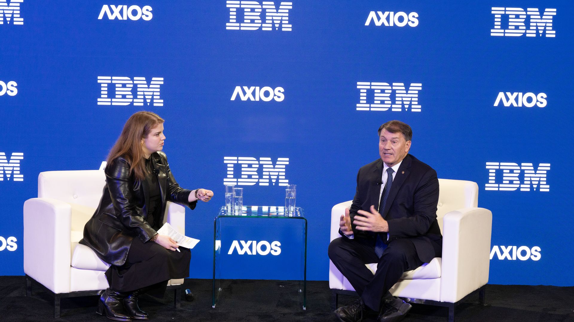 Two people sit on two white chairs in conversation