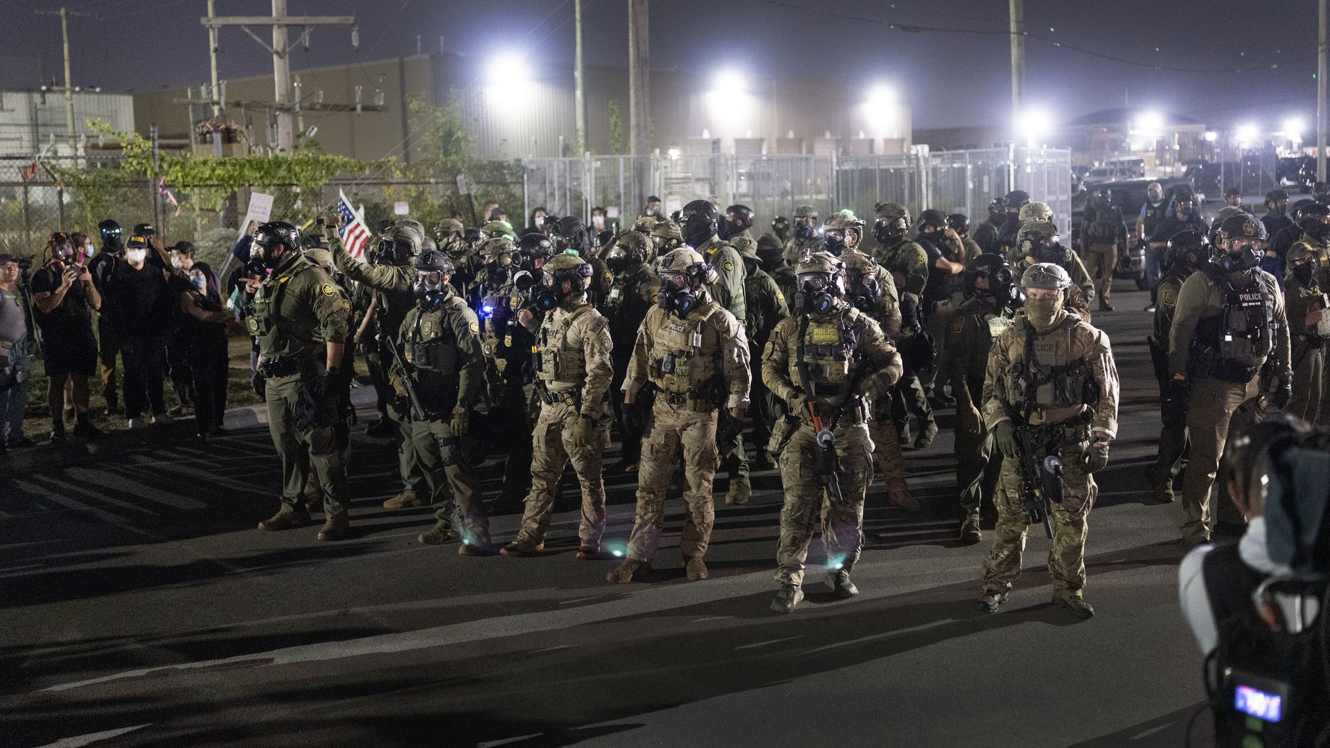 Photo of federal agents in uniforms with guns filing together outside of facility with flood lights blaring. 
