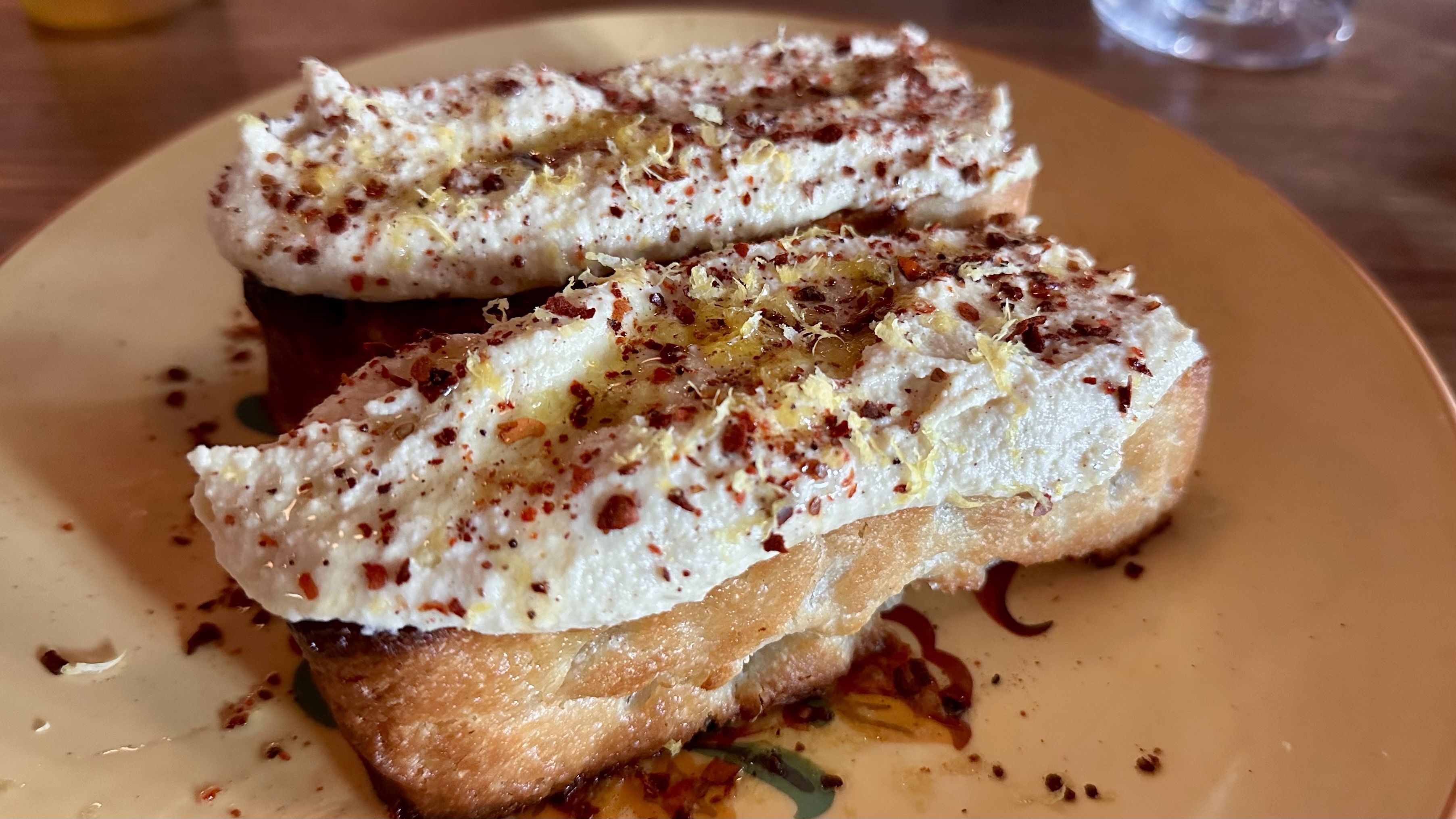 A photo of bread topped with hummus and red chili flakes and lemon zest