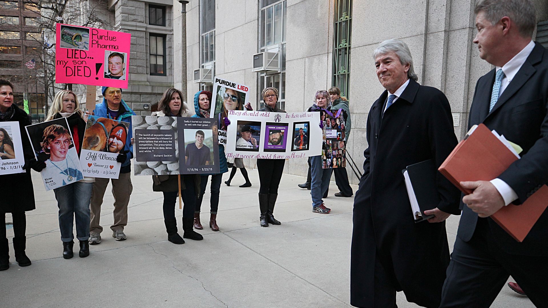 Two Purdue Pharma lawyers walk past protestors outside a courthouse. 