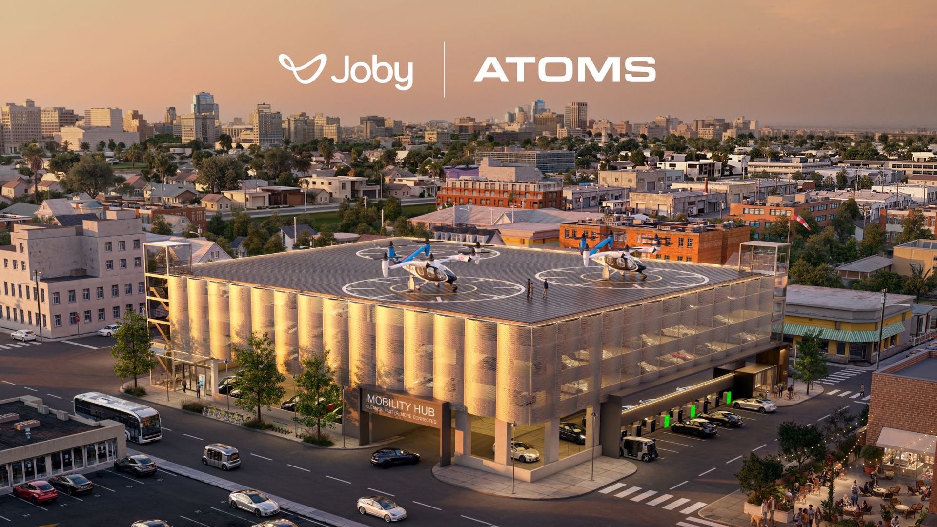 Sunset cityscape with a rooftop helipad housing two small helicopters. Prominent "Joby" and "ATOMS" branding across the skyline; busy streets, low-rise buildings, and pedestrians below.