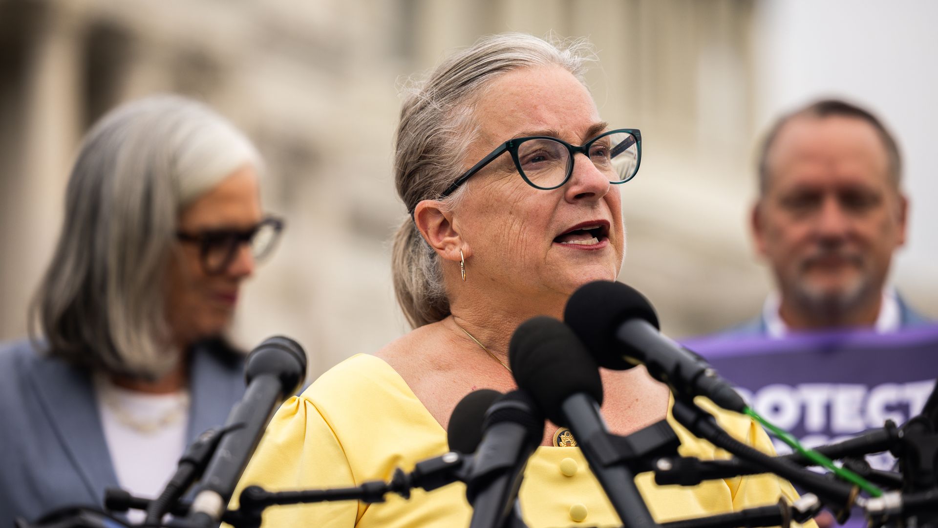 Rep. Susan Wild, wearing a yellow dress and speaking into microphones.