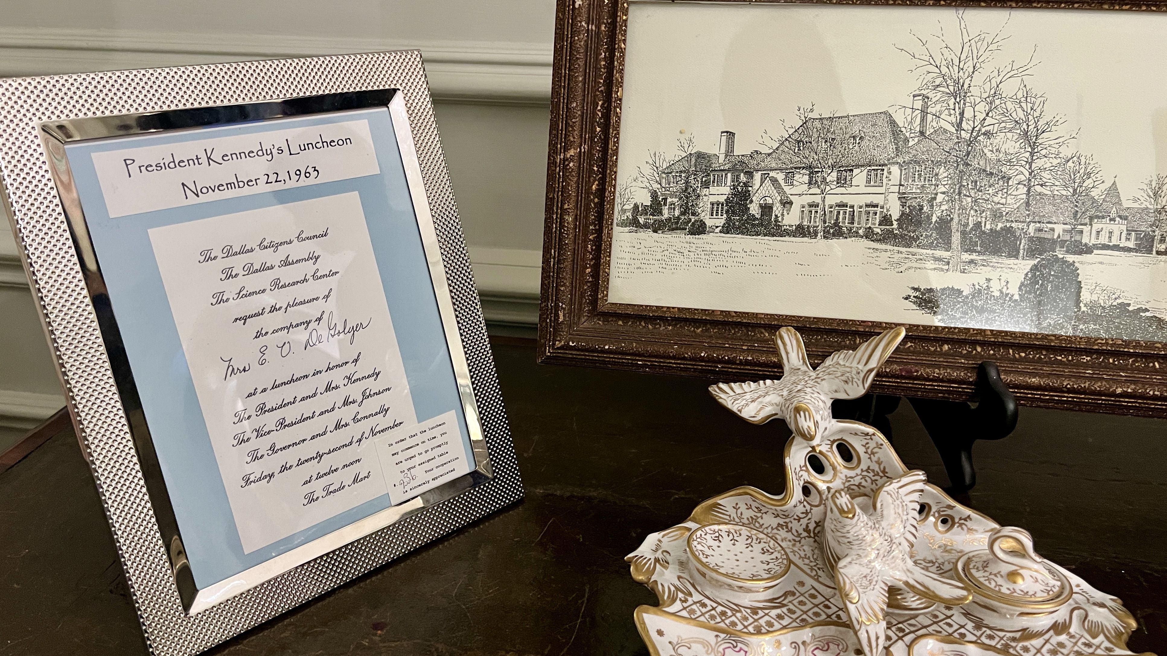 A framed invitation next to a framed sketch of a house