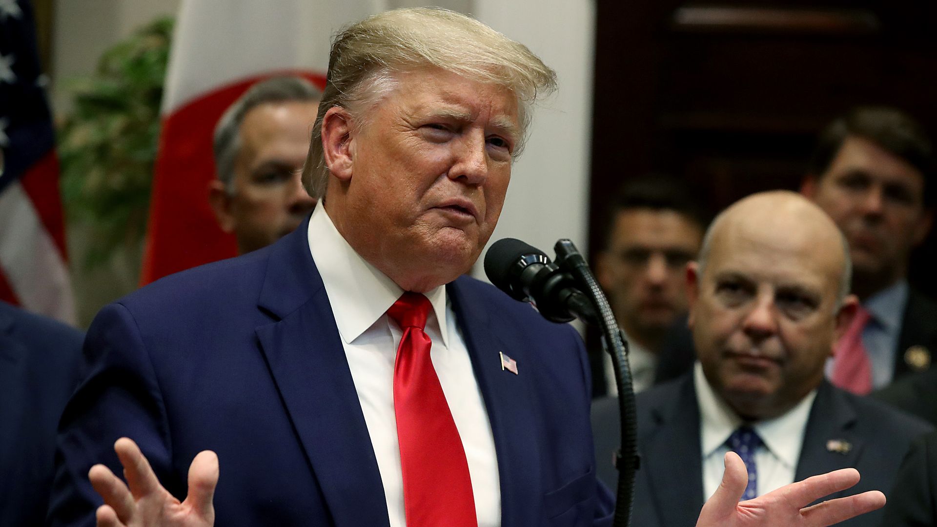 Trump gestures with his hands at a podium while a person stands behind him.