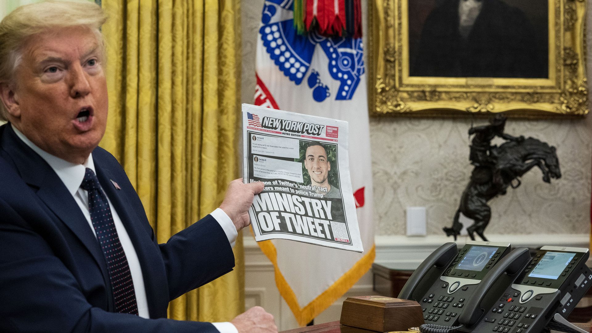 President Donald Trump holds up a newspaper with a photo of a Twitter executive as he discusses a social media executive order in the Oval Office.