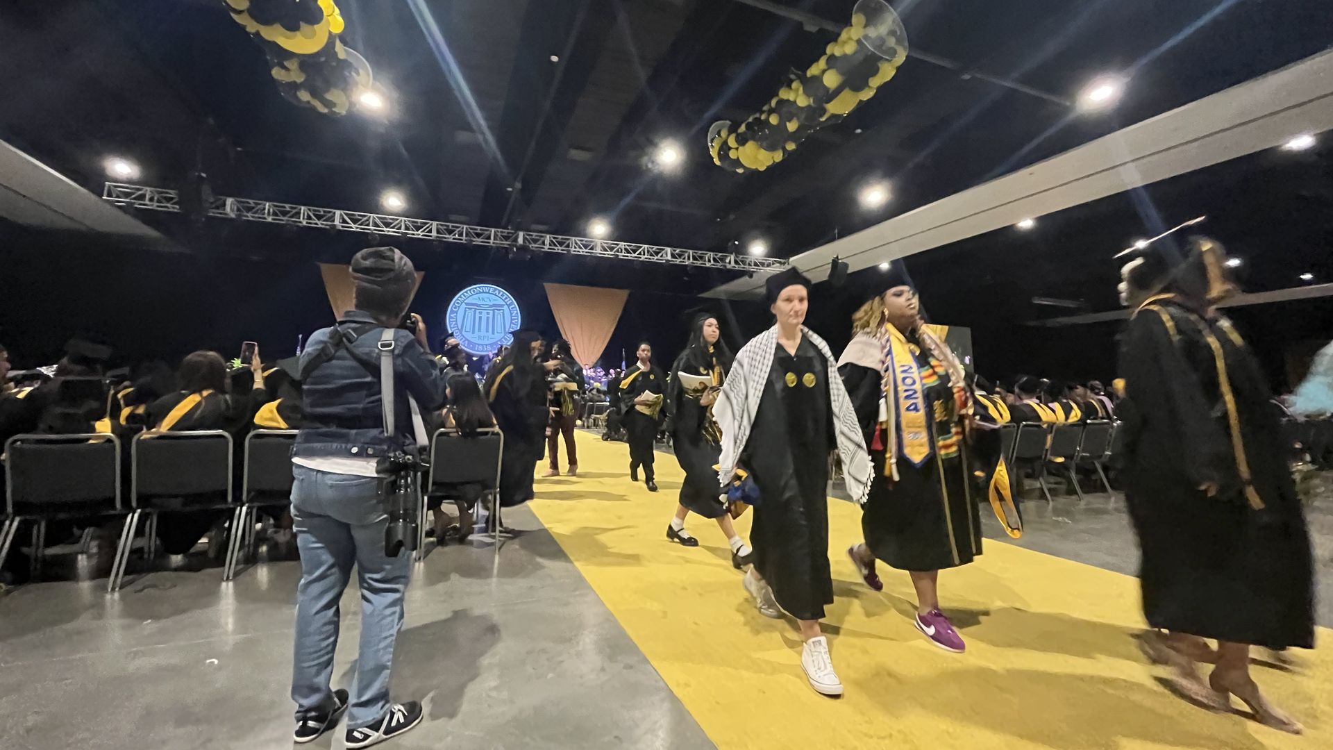 A few dozen graduates walk out in their robes