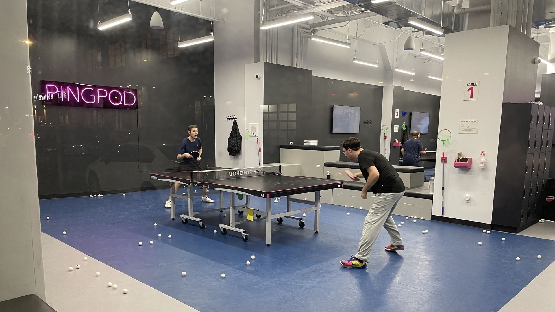 Two men play pingpong at an indoor pingpong table rental store.