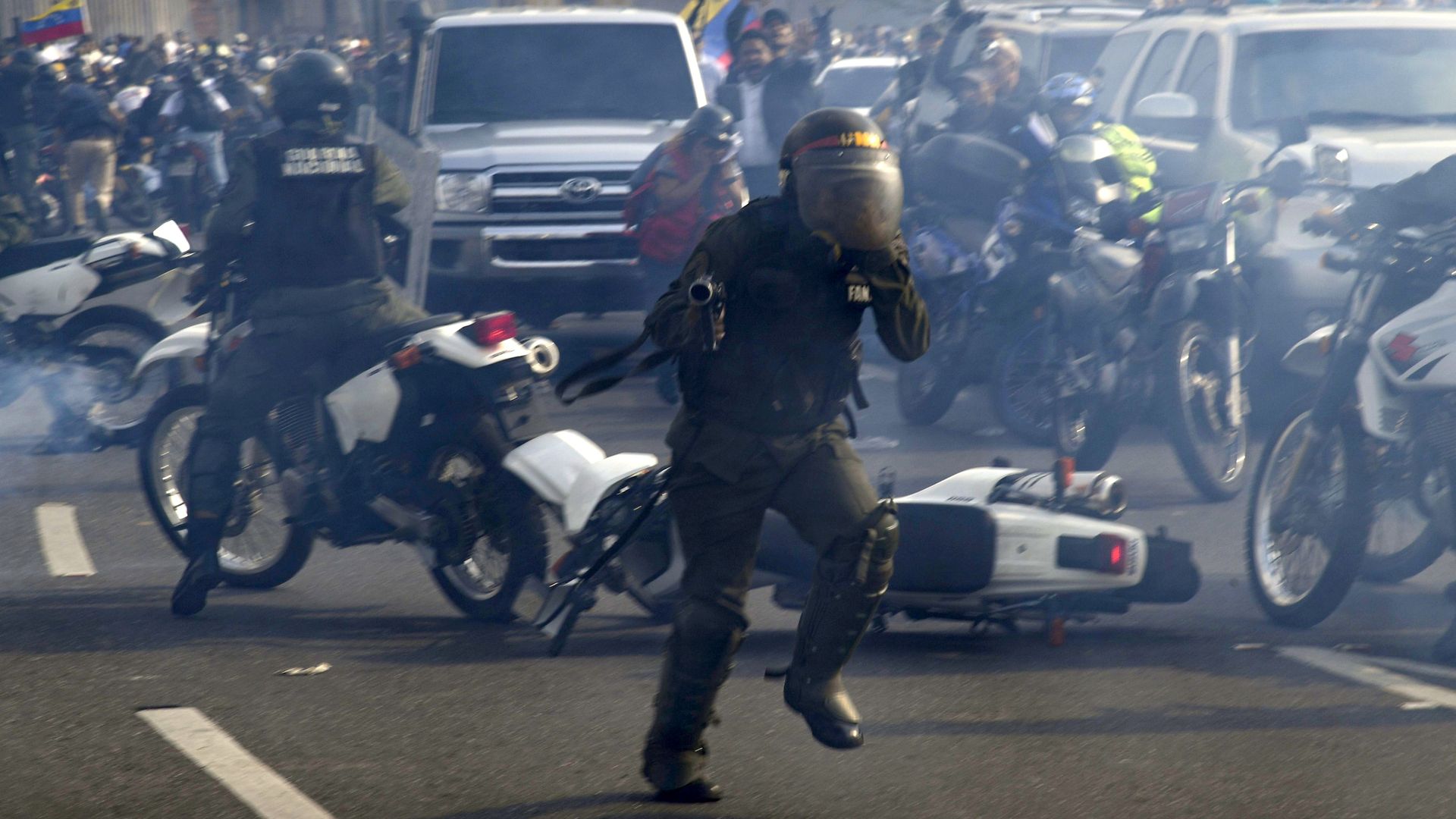 Members of the Bolivarian National Guard loyal to Venezuelan President Nicolas Maduro run under a cloud of tear gas after being repelled by guards supporting Venezuelan opposition leader. 