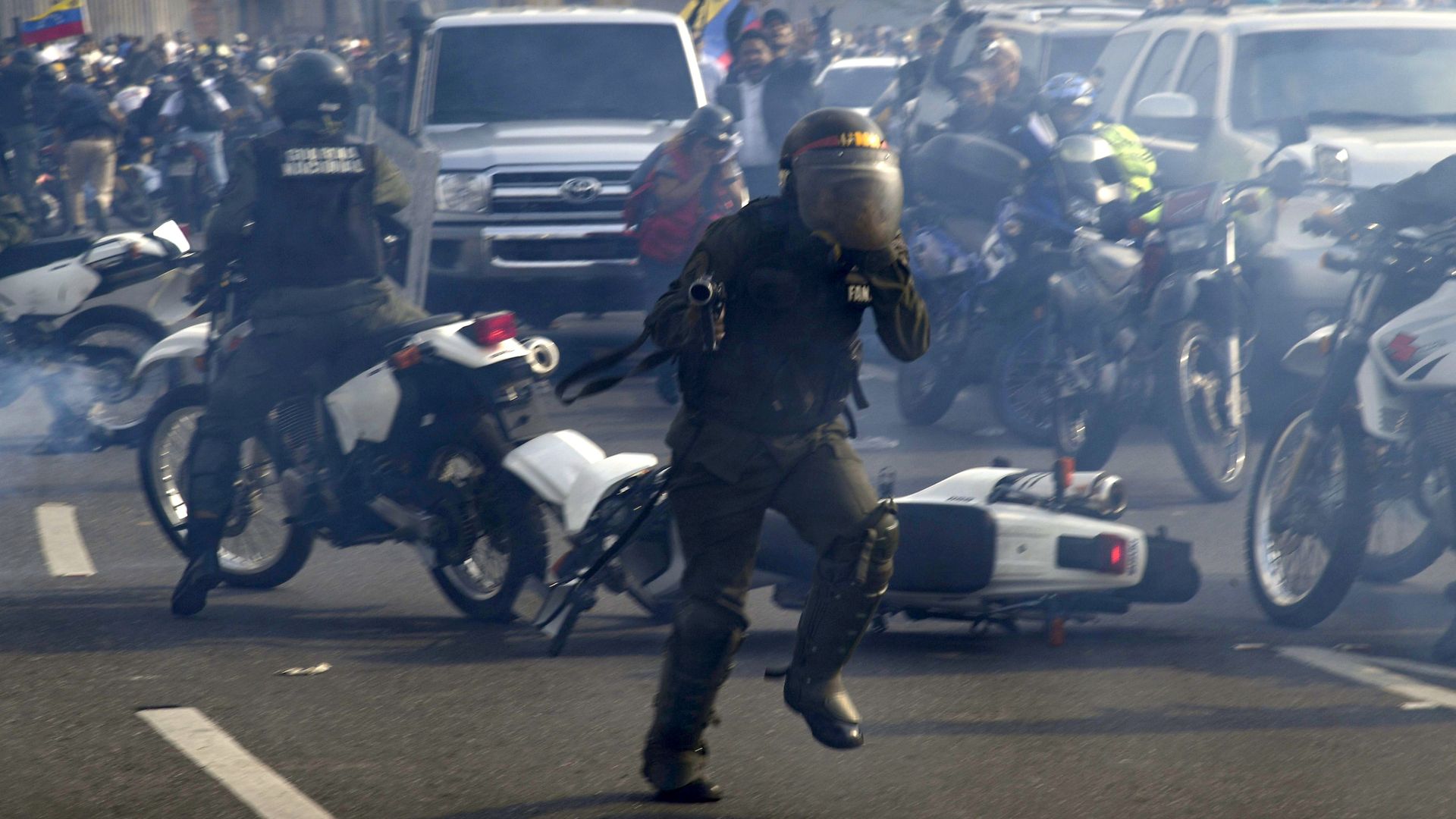 Members of the Bolivarian National Guard loyal to Venezuelan President Nicolas Maduro run under a cloud of tear gas after being repelled by guards supporting Venezuelan opposition leader.