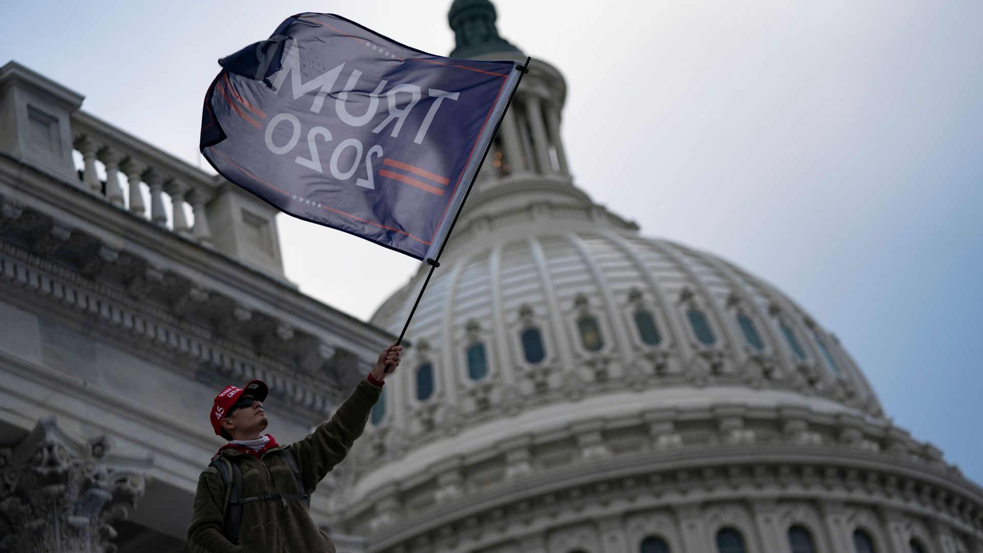 Photo of a Trump supporter waving a Trump 2020 flag in front of the Capitol building
