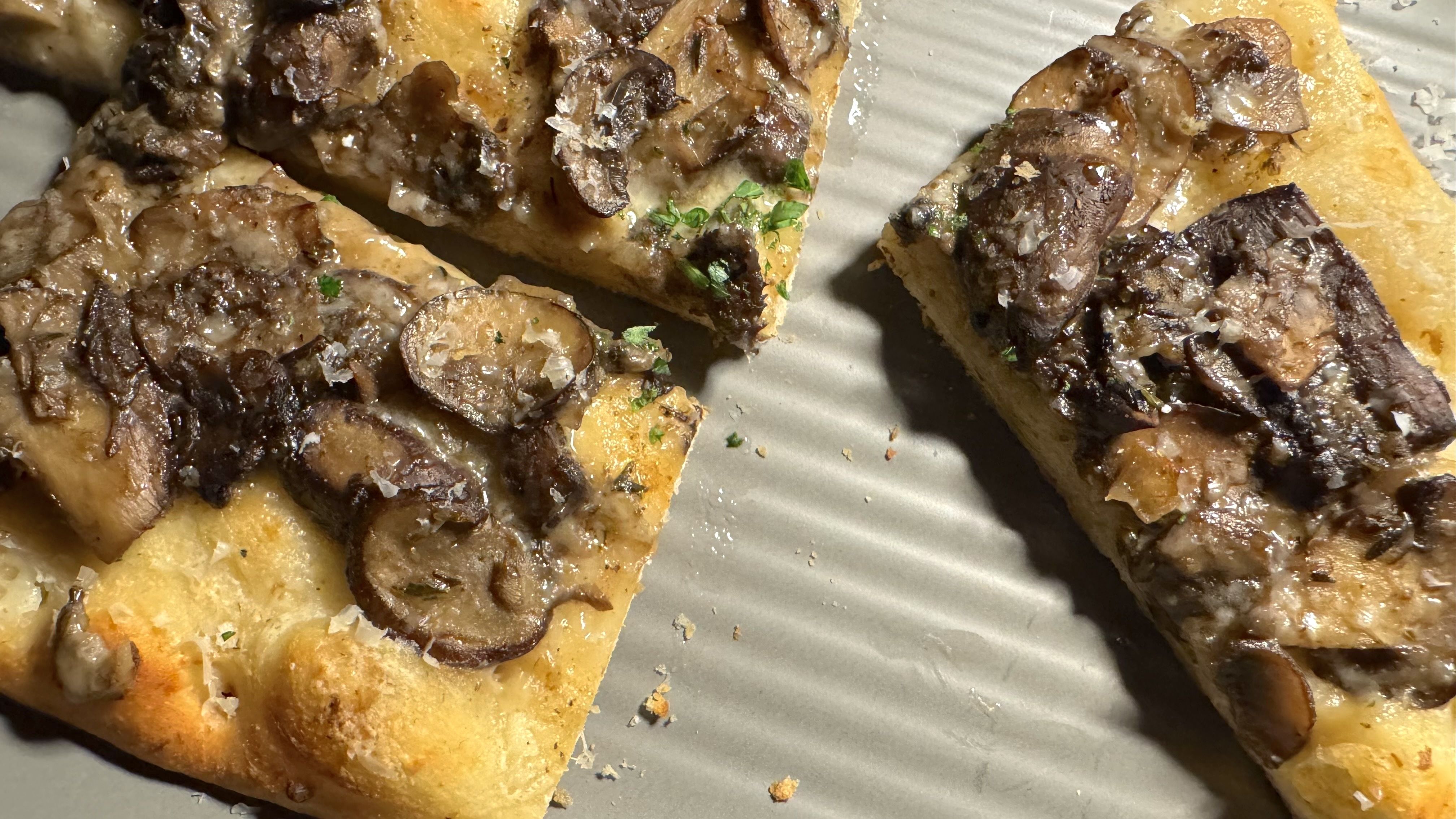 Close-up of sliced flatbread topped with sautéed mushrooms, herbs, and melted cheese on a ridged baking tray.