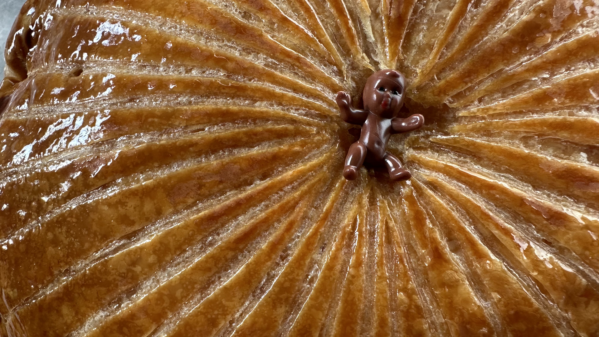 A king cake baby rests at the center of a galette-style king cake.