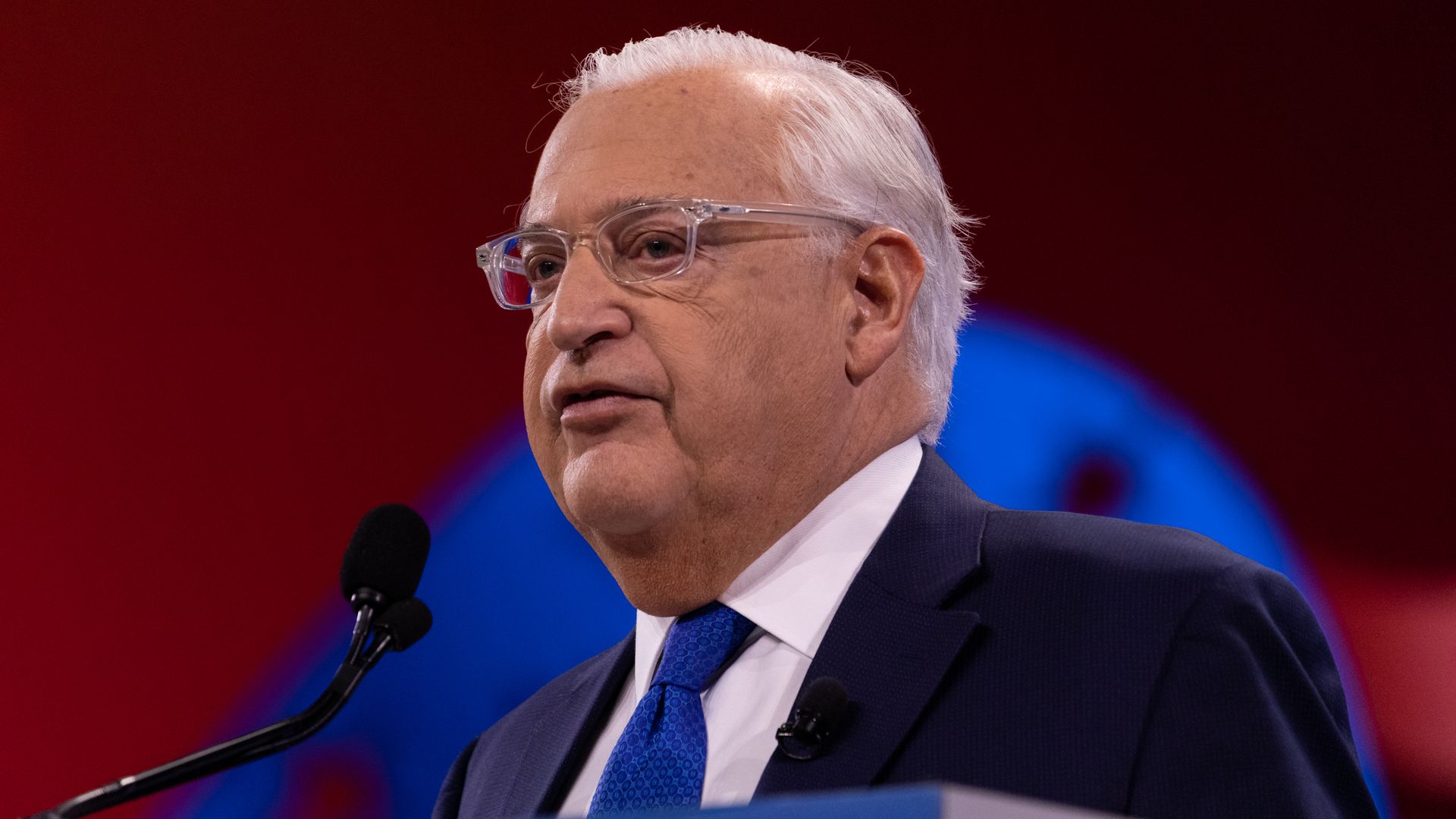 In this image, David Friedman faces the left and speaks, wearing glasses.